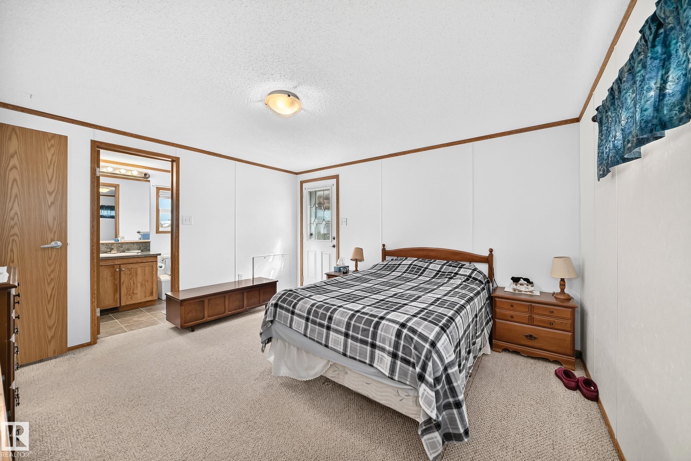 Spacious bedroom featuring neutral carpeting, a ceiling-mounted light fixture, and a white paneled wall finish with wood trim - #225 3400 48 St, Stony Plain, AB - Indoor Photo Showing Bedroom