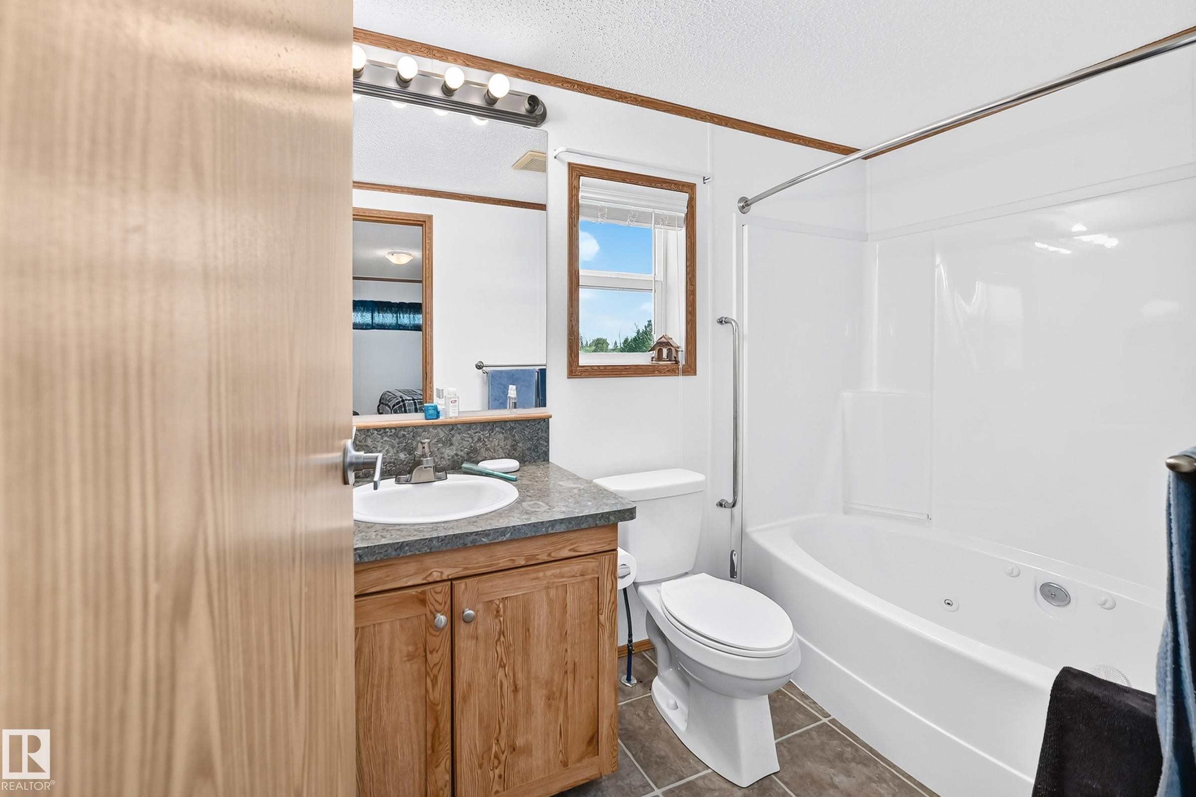 Bathroom featuring a wood-finish vanity with a built-in sink, a speckled countertop, and a white shower-tub combination with jets - #225 3400 48 St, Stony Plain, AB - Indoor Photo Showing Bathroom