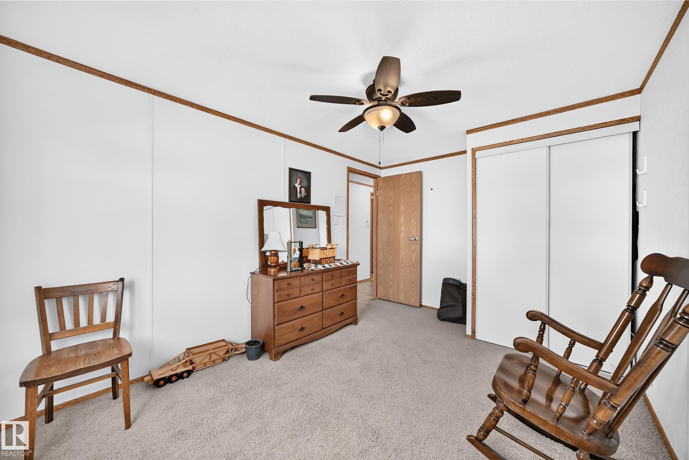 Carpeted room featuring a ceiling fan with integrated lighting, wood-finish trim, and sliding closet doors - #225 3400 48 St, Stony Plain, AB - Indoor
