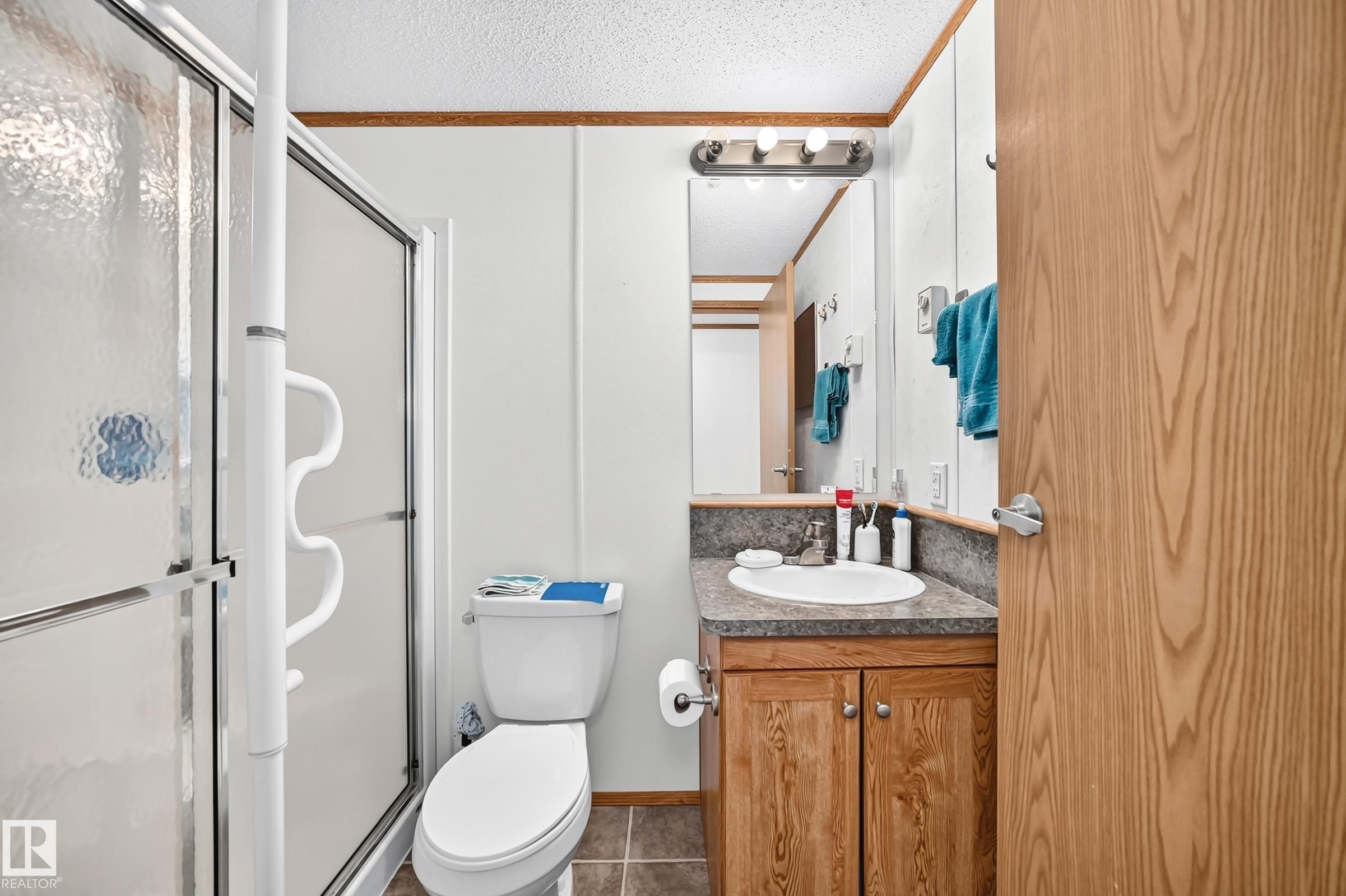 Shower with a textured glass enclosure and white grab bars, complemented by a wood-finish vanity with an integrated sink and a neutral-toned countertop - #225 3400 48 St, Stony Plain, AB - Indoor Photo Showing Bathroom