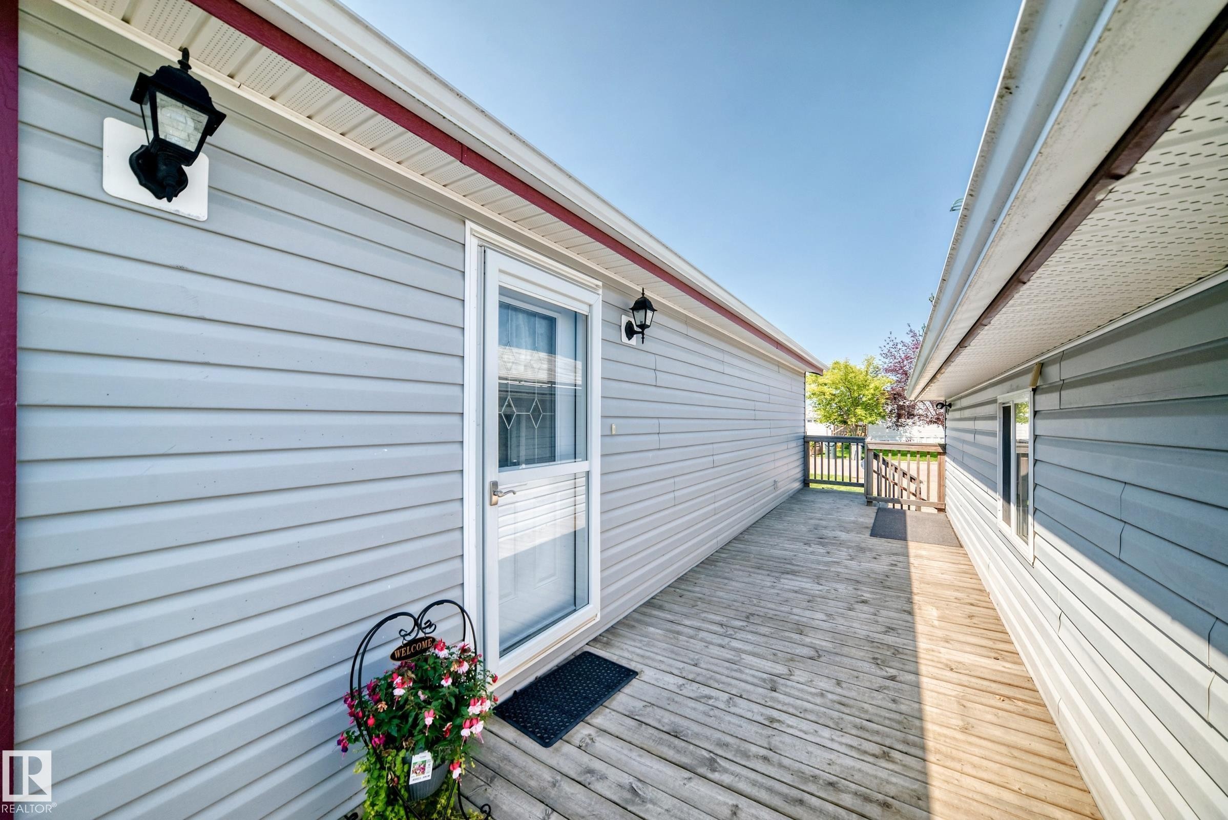 Exterior deck with wood-finish flooring, light grey horizontal siding, and a white screen door - #225 3400 48 St, Stony Plain, AB - Outdoor With Exterior