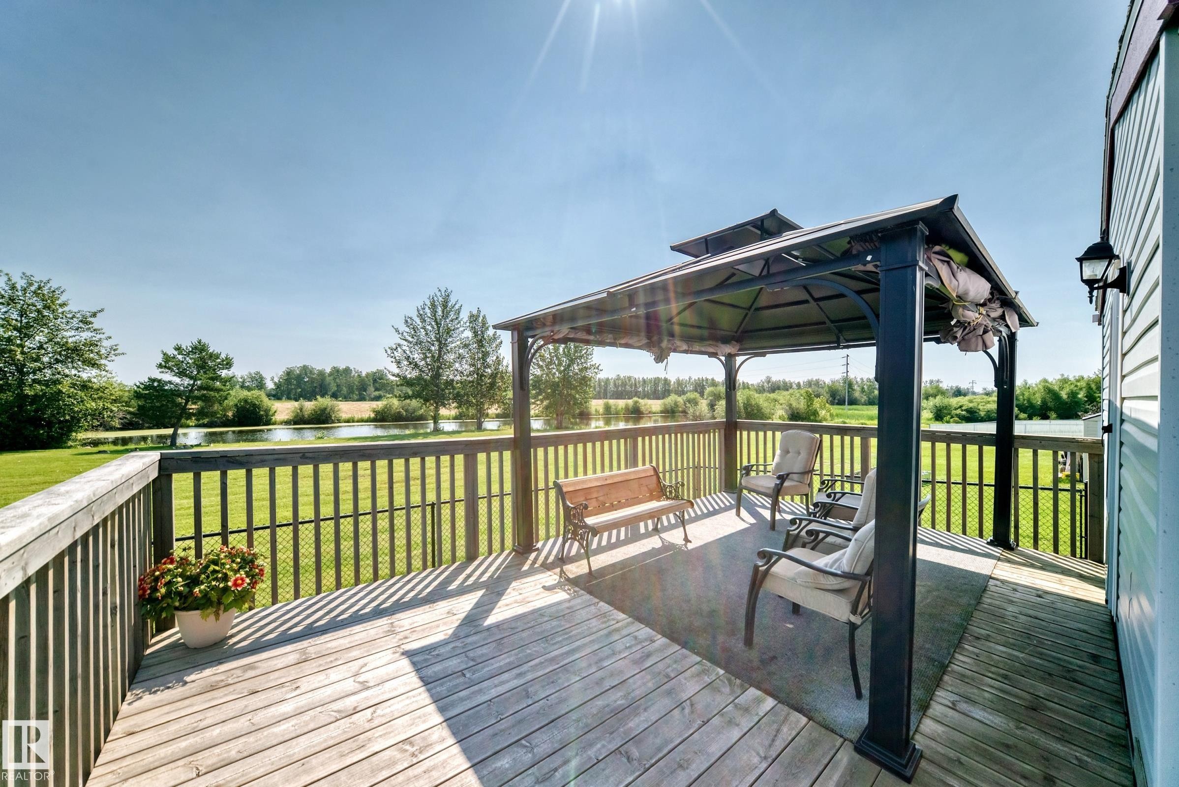Expansive wooden deck featuring a metal gazebo, black railing, and a wall-mounted exterior light fixture - #225 3400 48 St, Stony Plain, AB - Outdoor With Deck Patio Veranda With Exterior