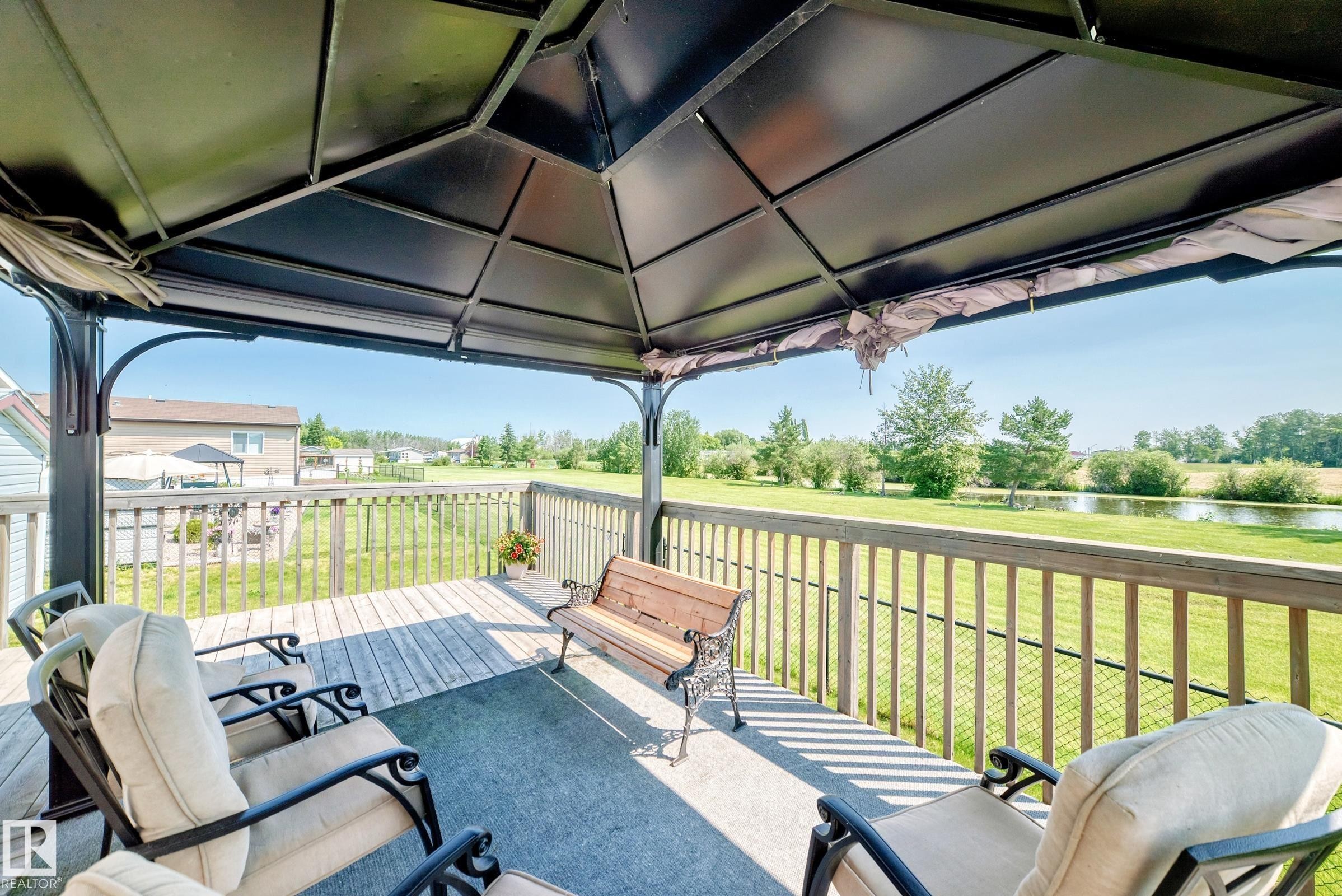 Expansive outdoor deck featuring a dark metal gazebo with a solid roof, wood plank flooring, a neutral-toned outdoor rug, and a wood railing - #225 3400 48 St, Stony Plain, AB - Outdoor With Deck Patio Veranda With Exterior