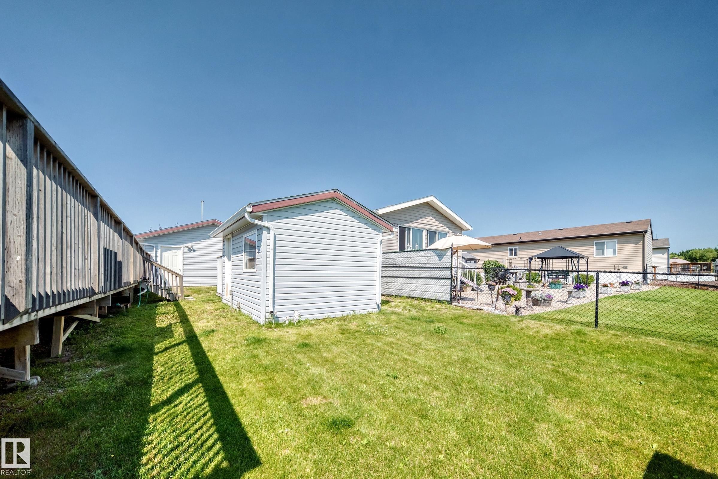 Spacious backyard featuring a manicured lawn, a detached storage shed, a black chain-link fence, a paved patio area, and a privacy fence - #225 3400 48 St, Stony Plain, AB - Outdoor With Exterior