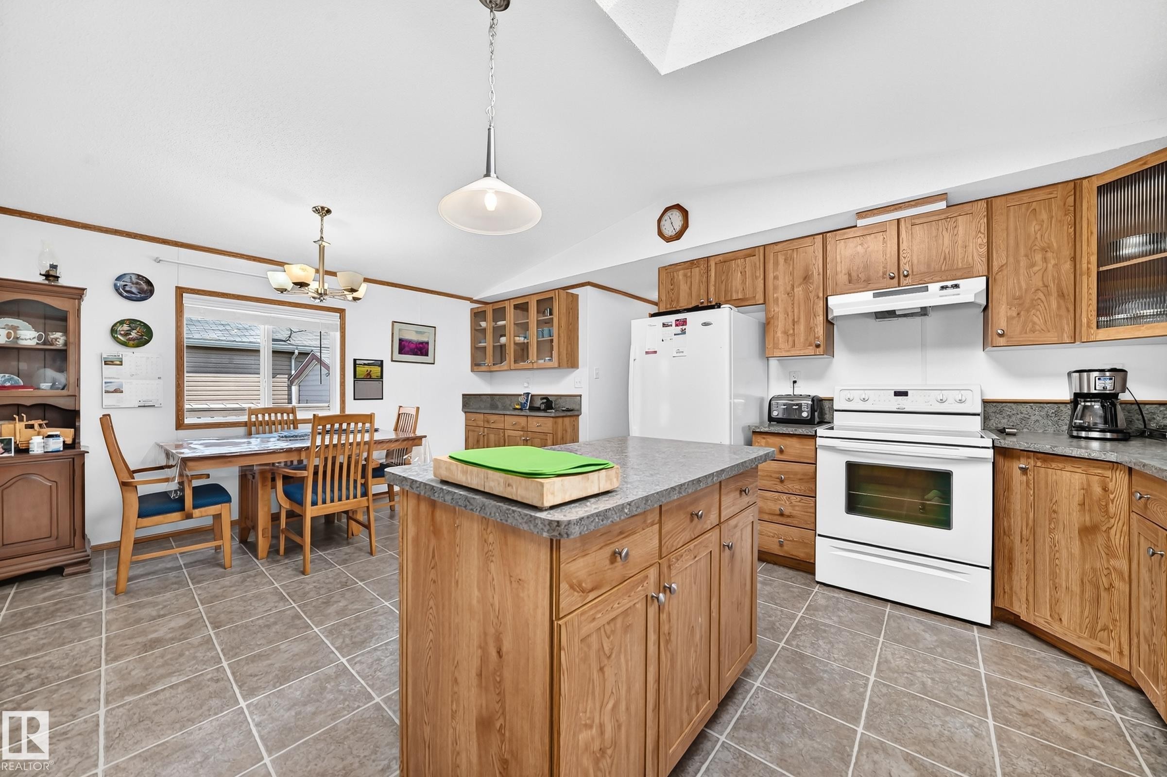 Kitchen featuring wood-finish cabinetry, a central island with a grey countertop, and tile flooring - #225 3400 48 St, Stony Plain, AB - Indoor Photo Showing Kitchen