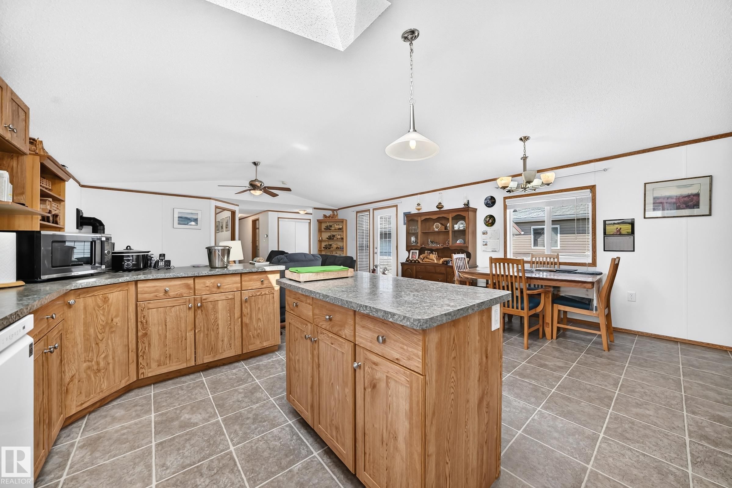 Open-concept kitchen and dining area featuring wood-finish cabinetry, a central island with a solid surface countertop, tiled flooring, and a skylight - #225 3400 48 St, Stony Plain, AB - Indoor Photo Showing Kitchen