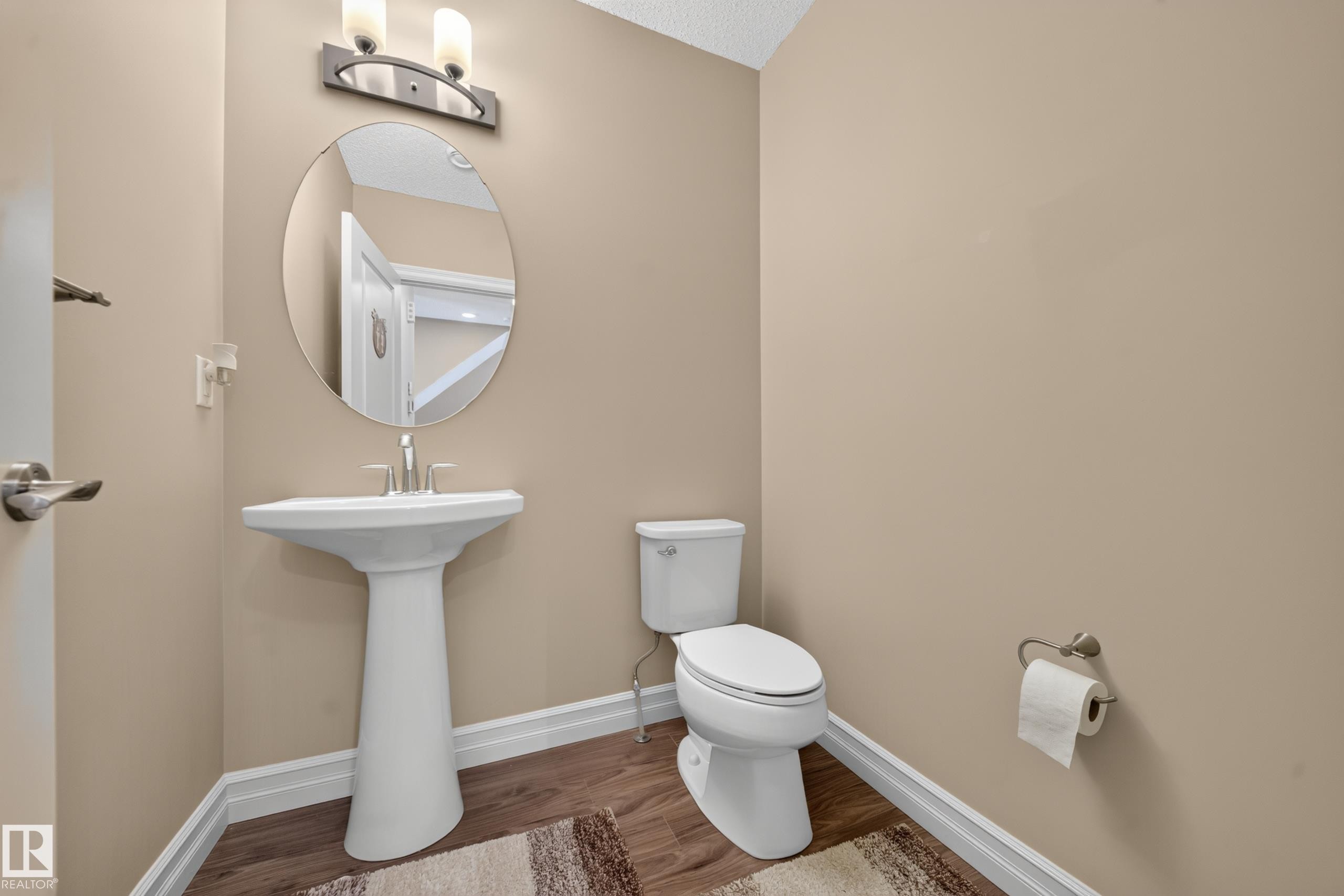 Powder room featuring a white pedestal sink with a brushed nickel faucet, an oval mirror, and a two-bulb wall sconce - #100 804 Welsh Dr Sw, Edmonton, AB - Indoor Photo Showing Bathroom