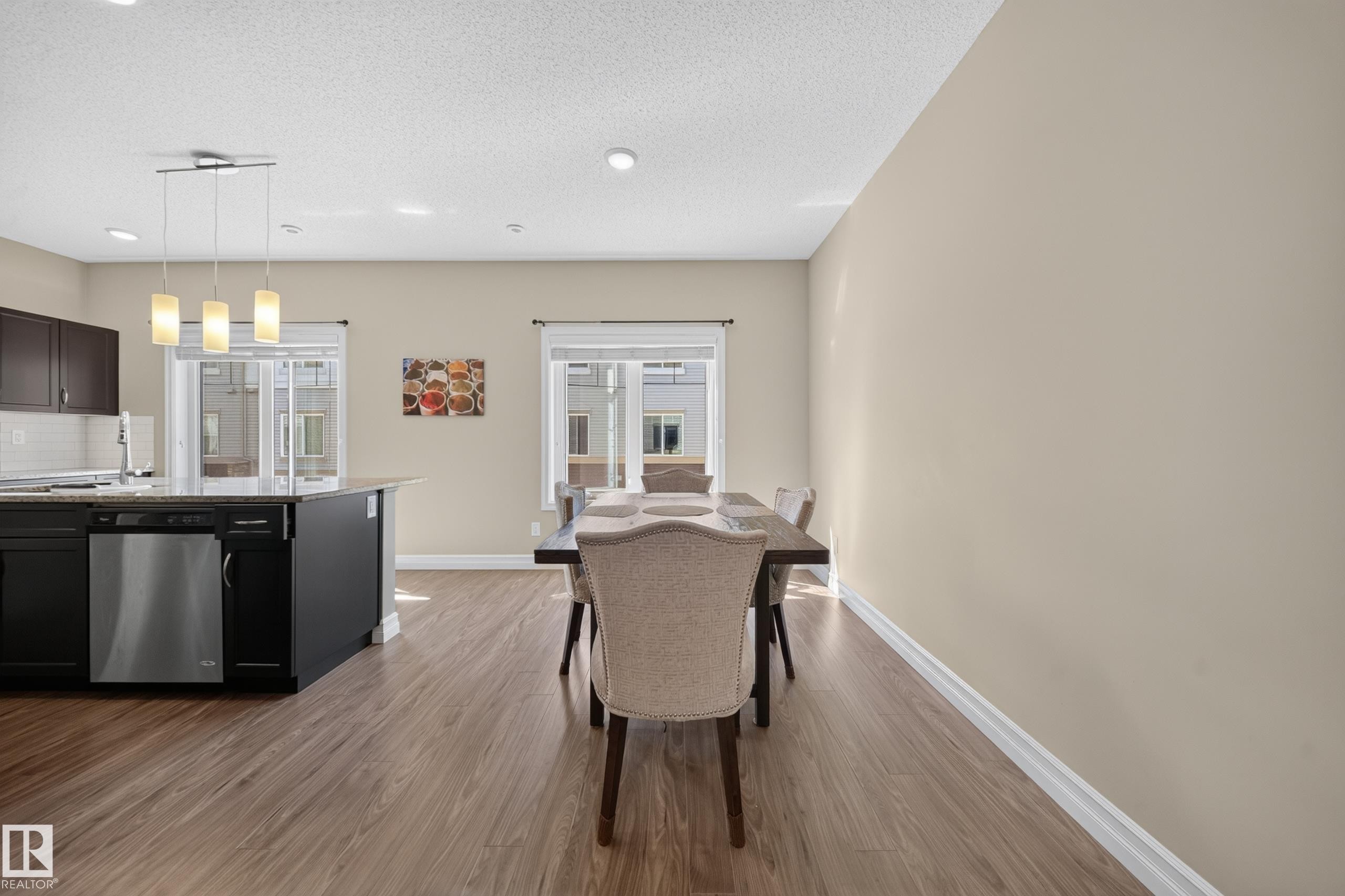Open-concept kitchen and dining area featuring wood-finish flooring, dark cabinetry, and light-toned walls - #100 804 Welsh Dr Sw, Edmonton, AB - Indoor