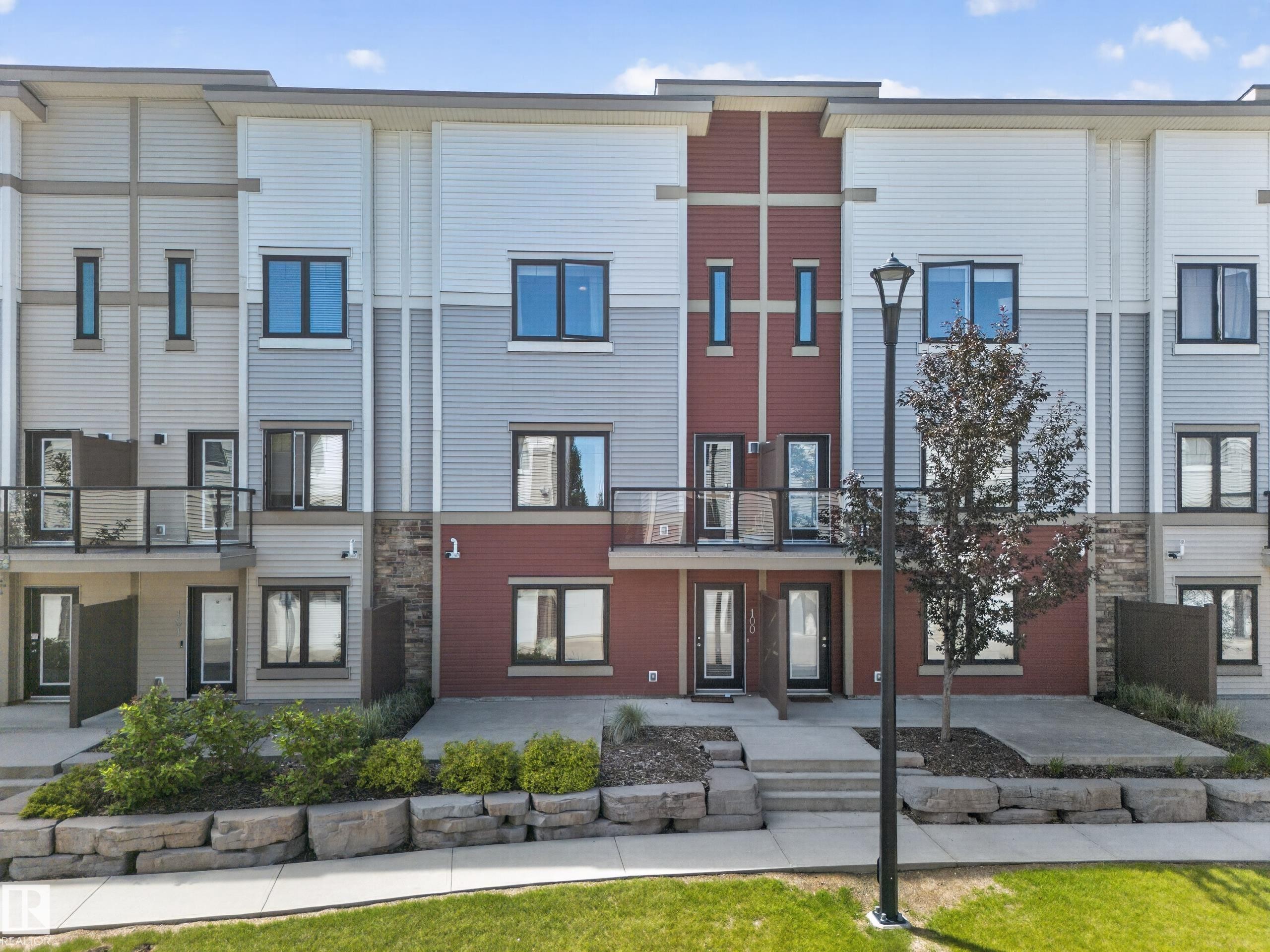 Modern townhome exterior featuring multi-toned siding, dark-framed windows, and a flat roofline - #100 804 Welsh Dr Sw, Edmonton, AB - Outdoor With Balcony With Facade