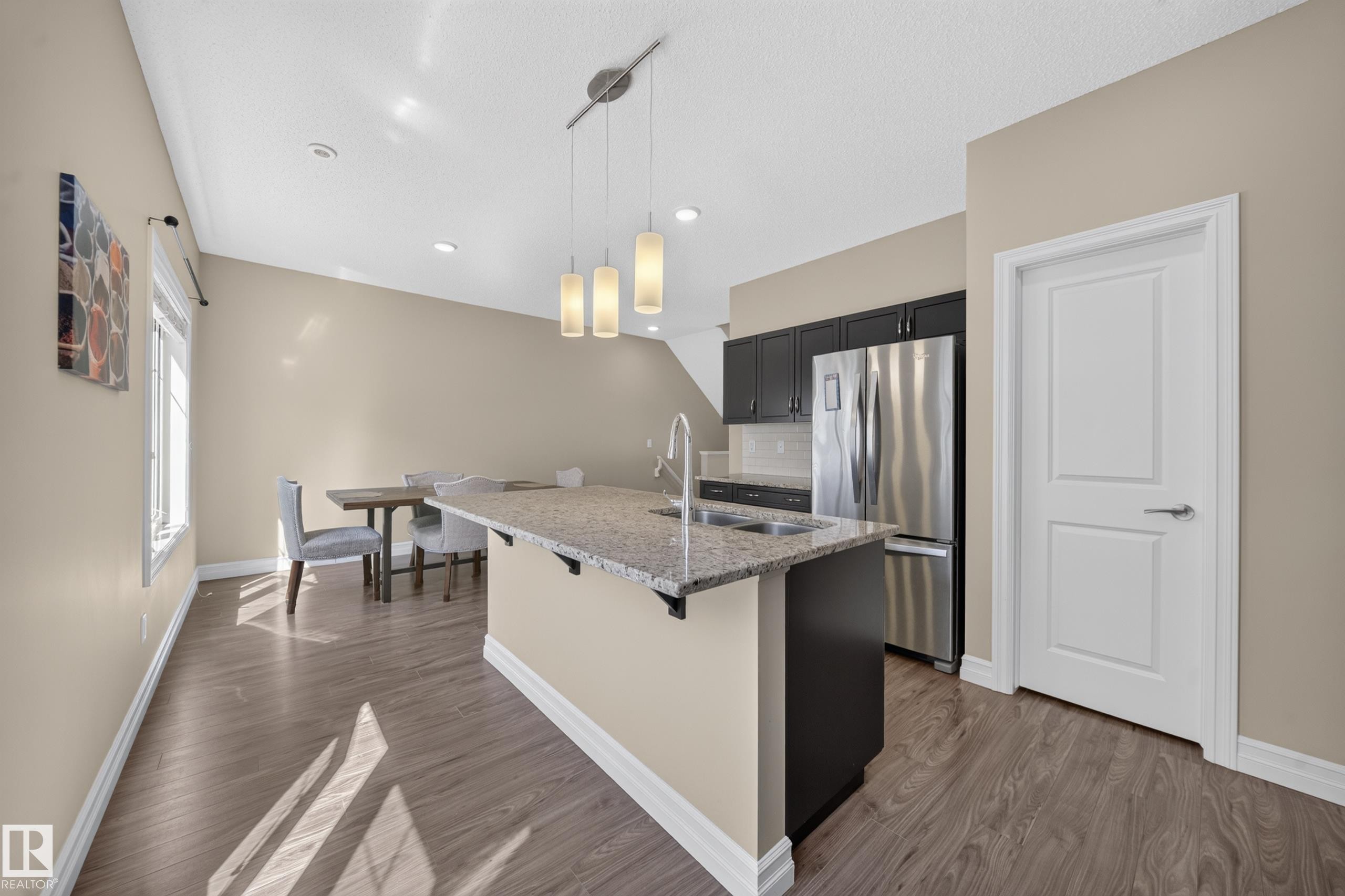 Kitchen island with a light-toned countertop, under-mount sink, and contemporary pendant lighting - #100 804 Welsh Dr Sw, Edmonton, AB - Indoor Photo Showing Kitchen With Stainless Steel Kitchen With Upgraded Kitchen