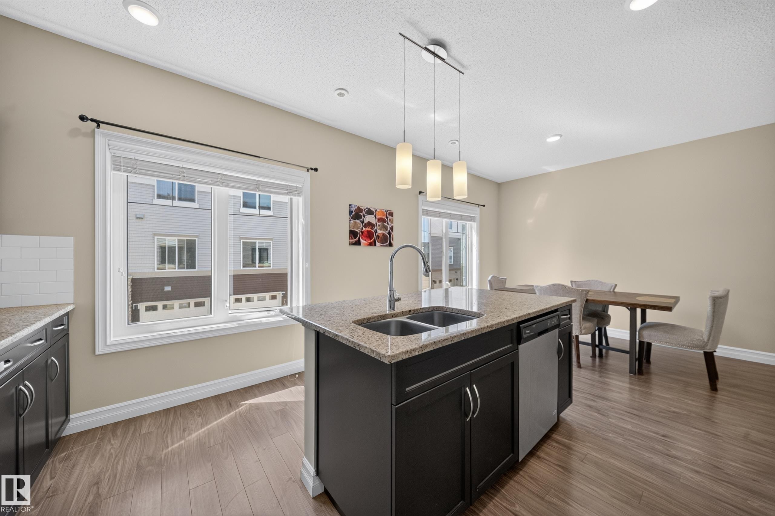 Kitchen island featuring a double-basin sink, granite-finish countertop, and integrated stainless-steel dishwasher - #100 804 Welsh Dr Sw, Edmonton, AB - Indoor Photo Showing Kitchen With Double Sink
