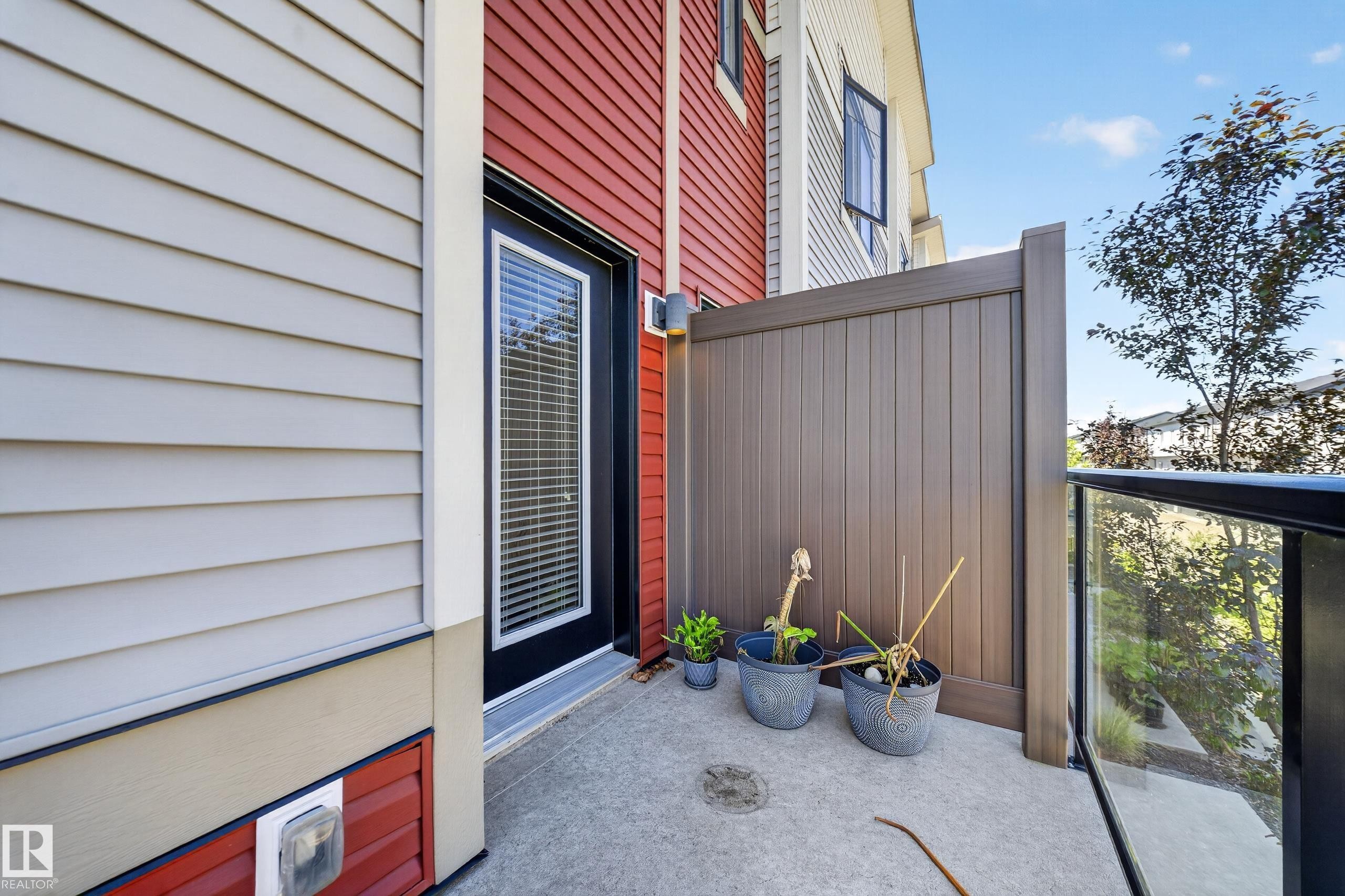 Private outdoor patio featuring a concrete surface, a partial privacy screen, and a glass railing - #100 804 Welsh Dr Sw, Edmonton, AB - Outdoor With Balcony With Exterior