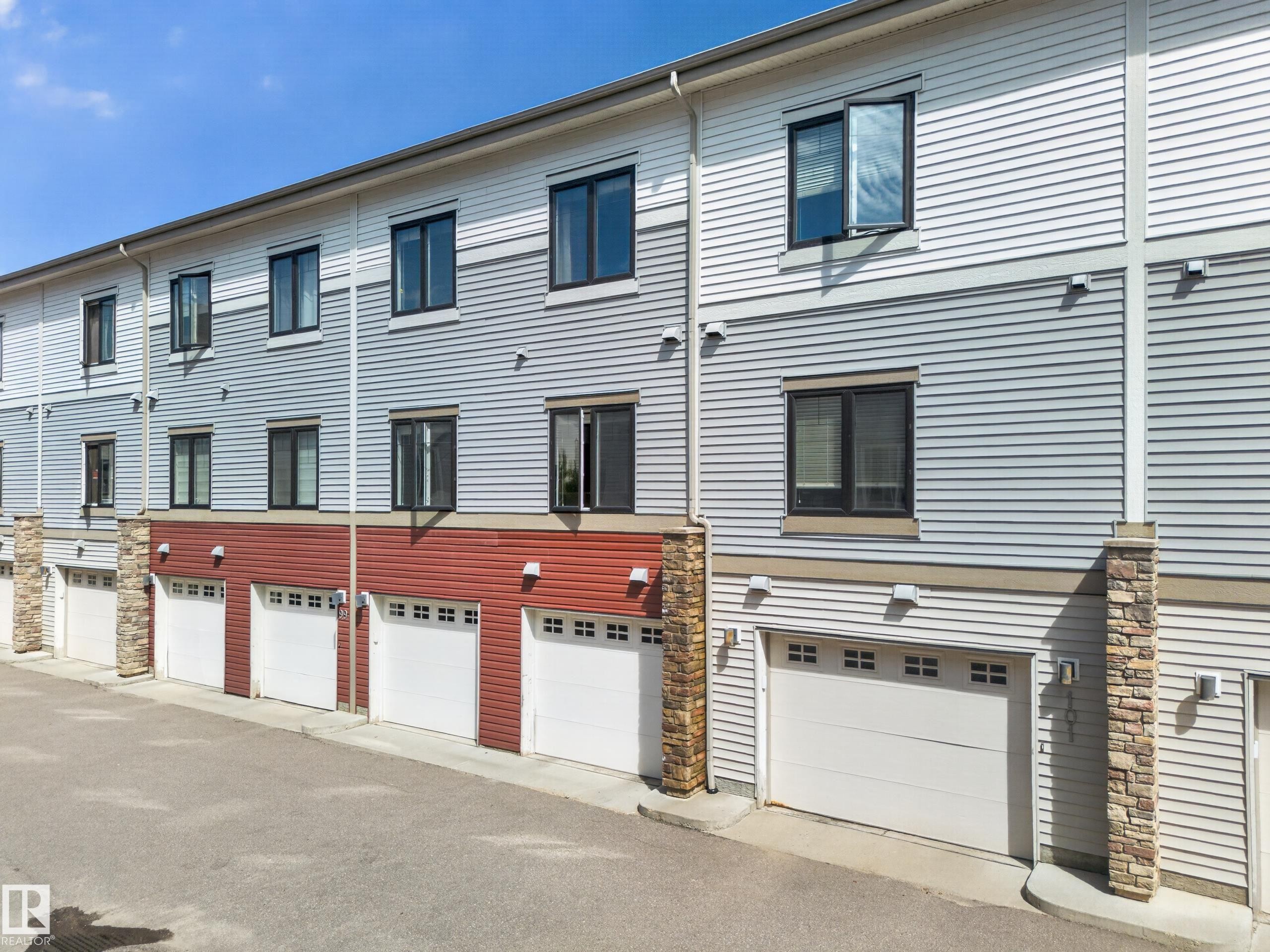 Modern multi-level townhome exteriors featuring horizontal siding in white and gray tones, red accent siding, and stone pillar details - #100 804 Welsh Dr Sw, Edmonton, AB - Outdoor With Exterior