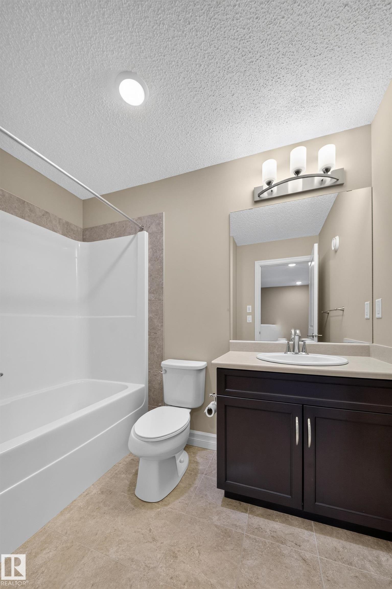 Bathroom featuring a combined tub and shower unit with tile surround, a dark wood-finish vanity with a light countertop, an undermount sink, and tile flooring - #100 804 Welsh Dr Sw, Edmonton, AB - Indoor Photo Showing Bathroom