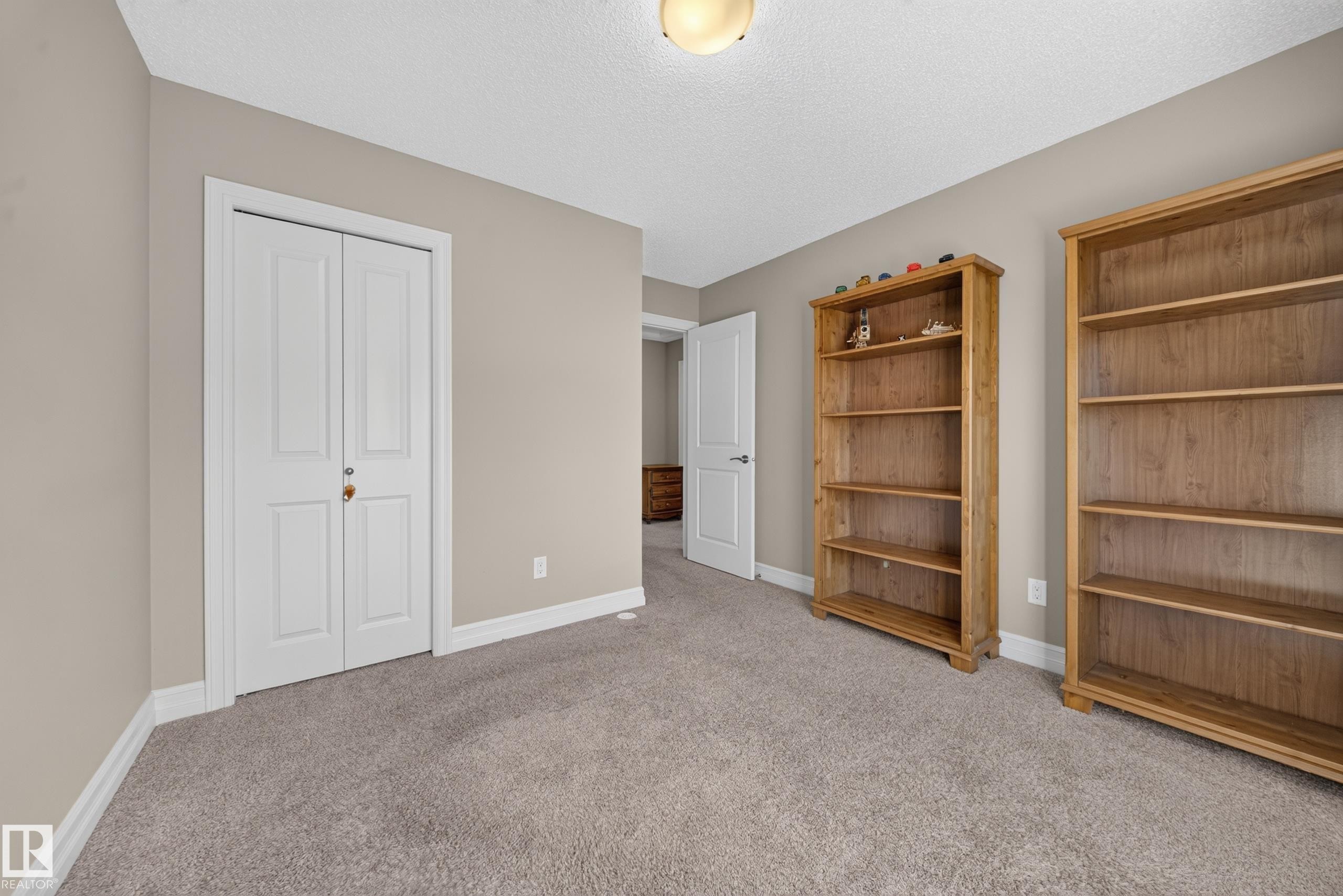 Neutral-toned room featuring a light brown carpet, white baseboards, and a white ceiling with a flush-mount light fixture - #100 804 Welsh Dr Sw, Edmonton, AB - Indoor