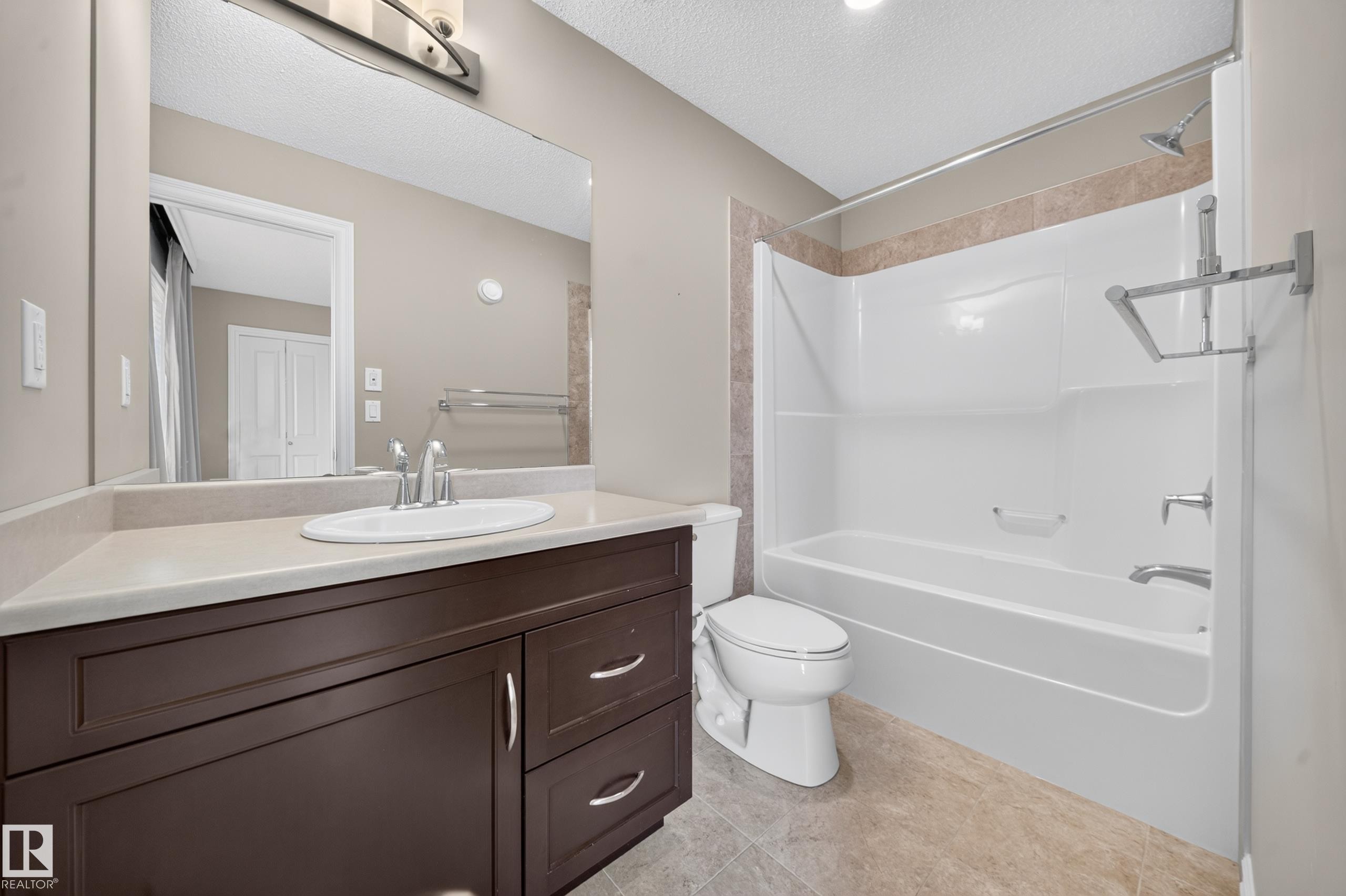 Bathroom featuring a dark wood-finish vanity with a light-toned countertop, an undermount sink, and a large wall-mounted mirror - #100 804 Welsh Dr Sw, Edmonton, AB - Indoor Photo Showing Bathroom