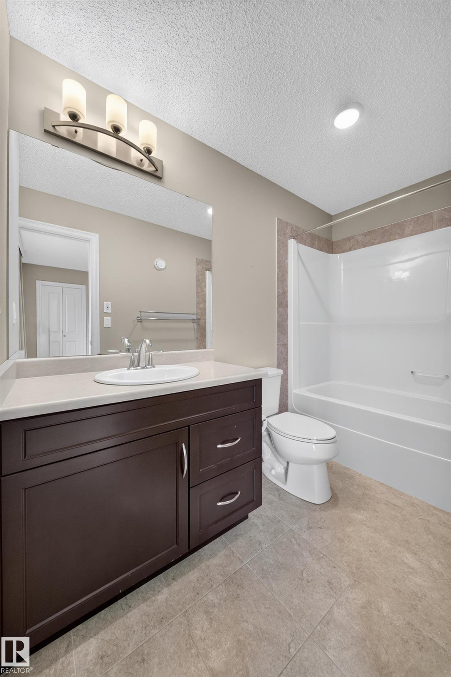 Bathroom featuring a dark wood-finish vanity with a light countertop, a rectangular mirror, and a three-light fixture - #100 804 Welsh Dr Sw, Edmonton, AB - Indoor Photo Showing Bathroom