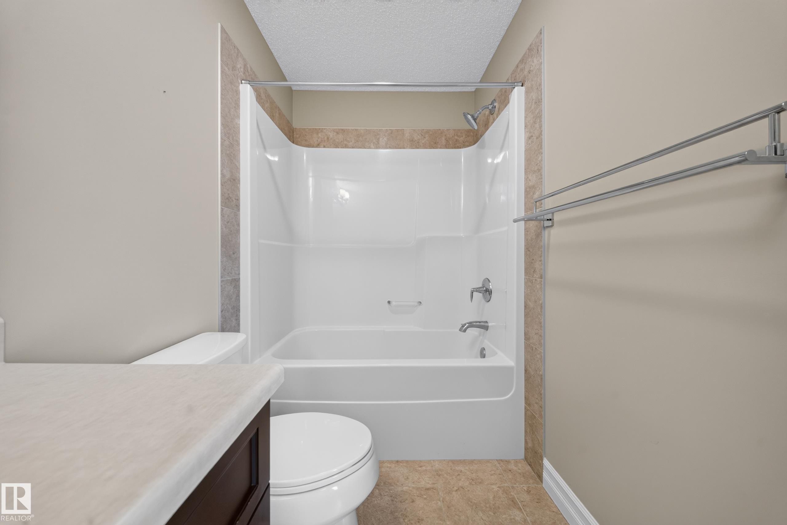 Bathroom featuring a white tub/shower combination with chrome fixtures, surrounded by a tiled accent wall - #100 804 Welsh Dr Sw, Edmonton, AB - Indoor Photo Showing Bathroom