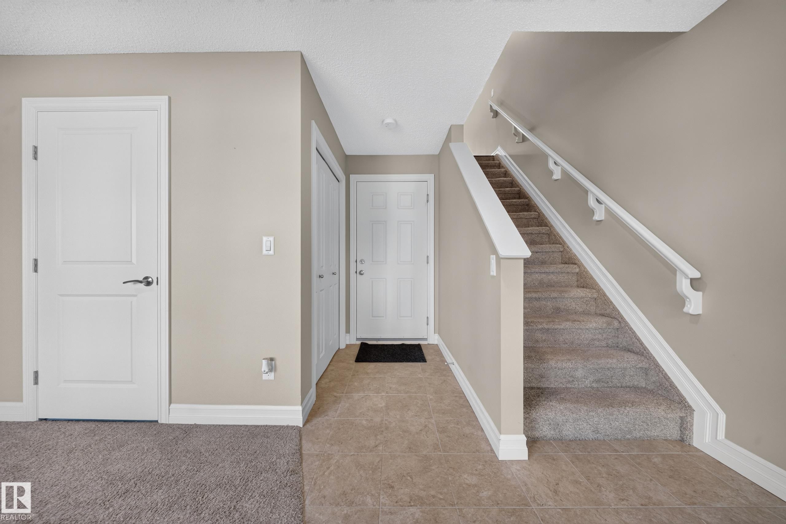 Foyer featuring neutral wall tones, white trim, and a carpeted staircase with white handrails - #100 804 Welsh Dr Sw, Edmonton, AB - Indoor Photo Showing Other Room