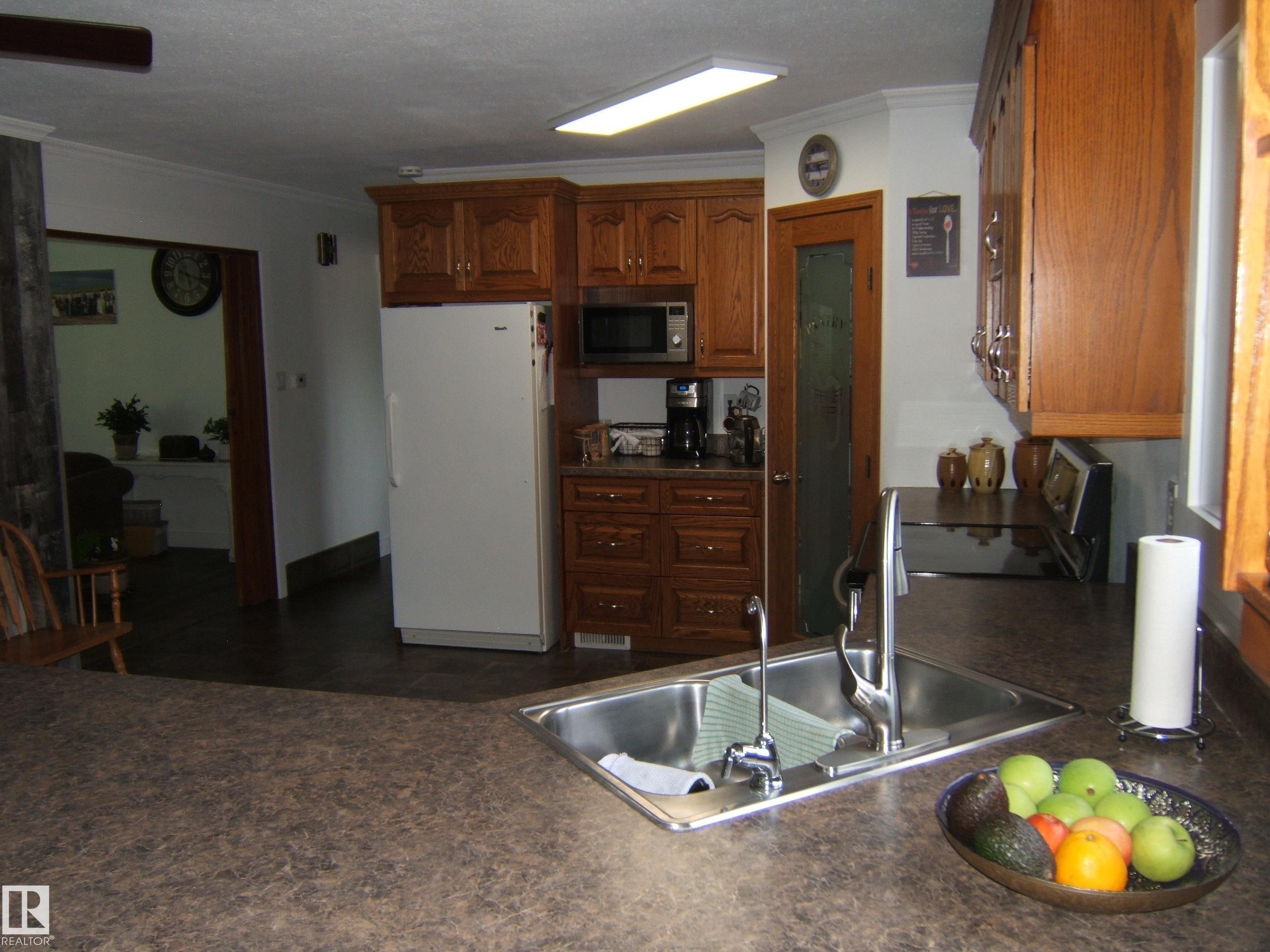 Kitchen featuring a double stainless steel sink with a high-arc faucet, wood-finish cabinetry, and laminate countertops - 151042 Twp Rd 562, Rural Two Hills County, AB - Indoor Photo Showing Kitchen With Double Sink