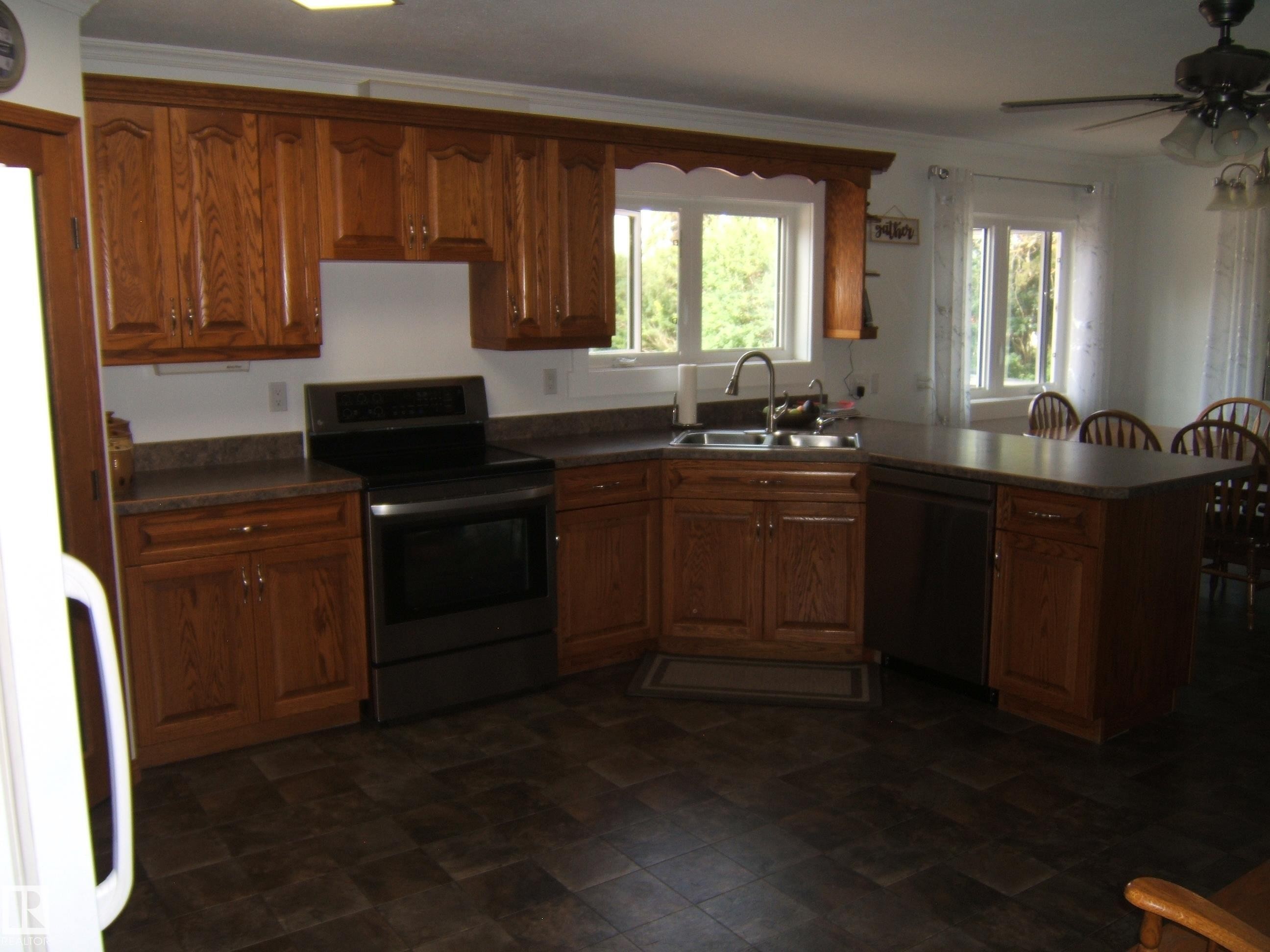 Kitchen featuring wood cabinetry, dark countertops, built-in sink, dark floor tiling, and a black range oven - 151042 Twp Rd 562, Rural Two Hills County, AB - Indoor Photo Showing Kitchen With Double Sink