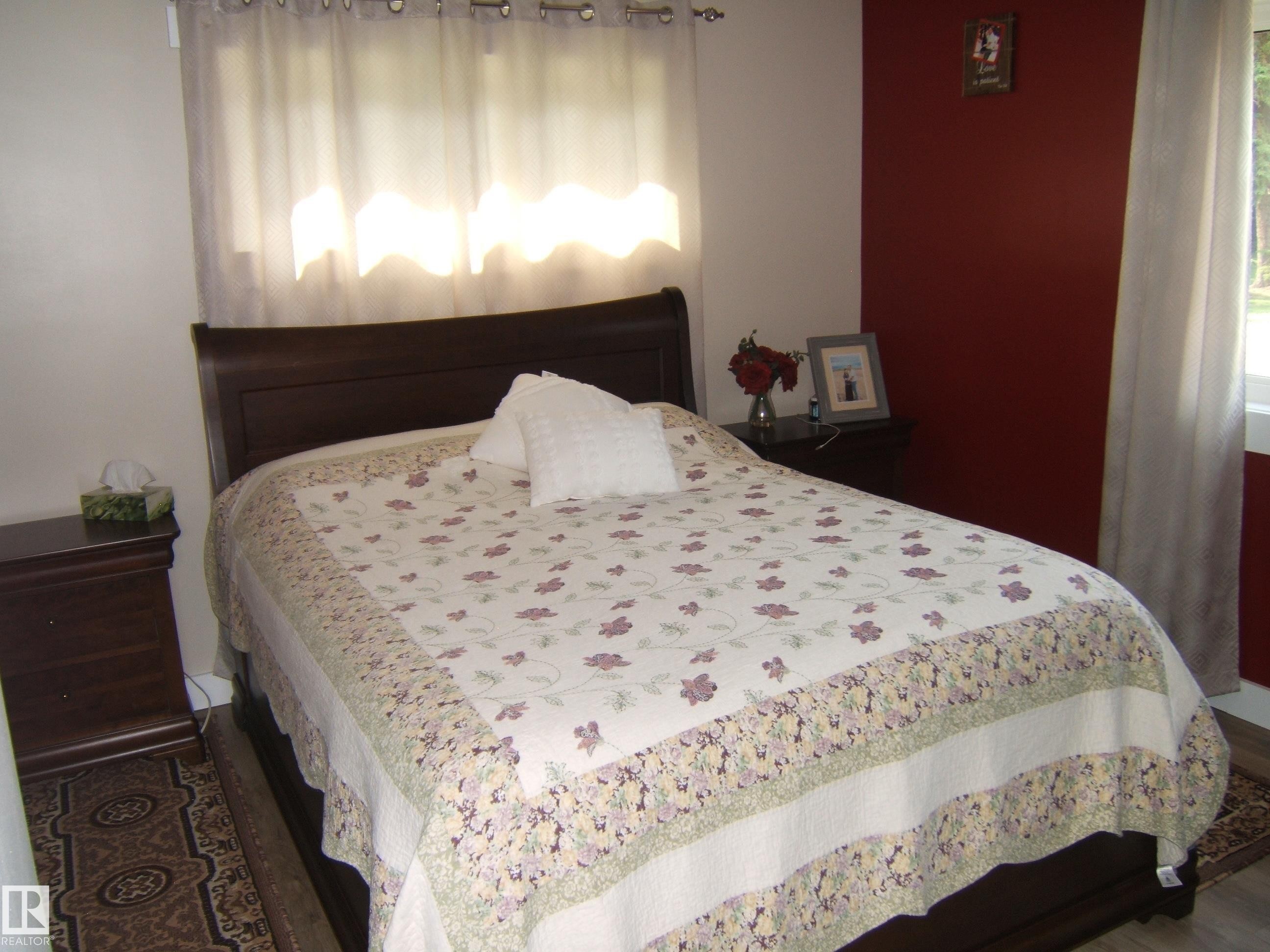 Interior space featuring wood-finish flooring, a window with sheer curtains, an accent wall with a deep red finish, and white painted walls - 151042 Twp Rd 562, Rural Two Hills County, AB - Indoor Photo Showing Bedroom