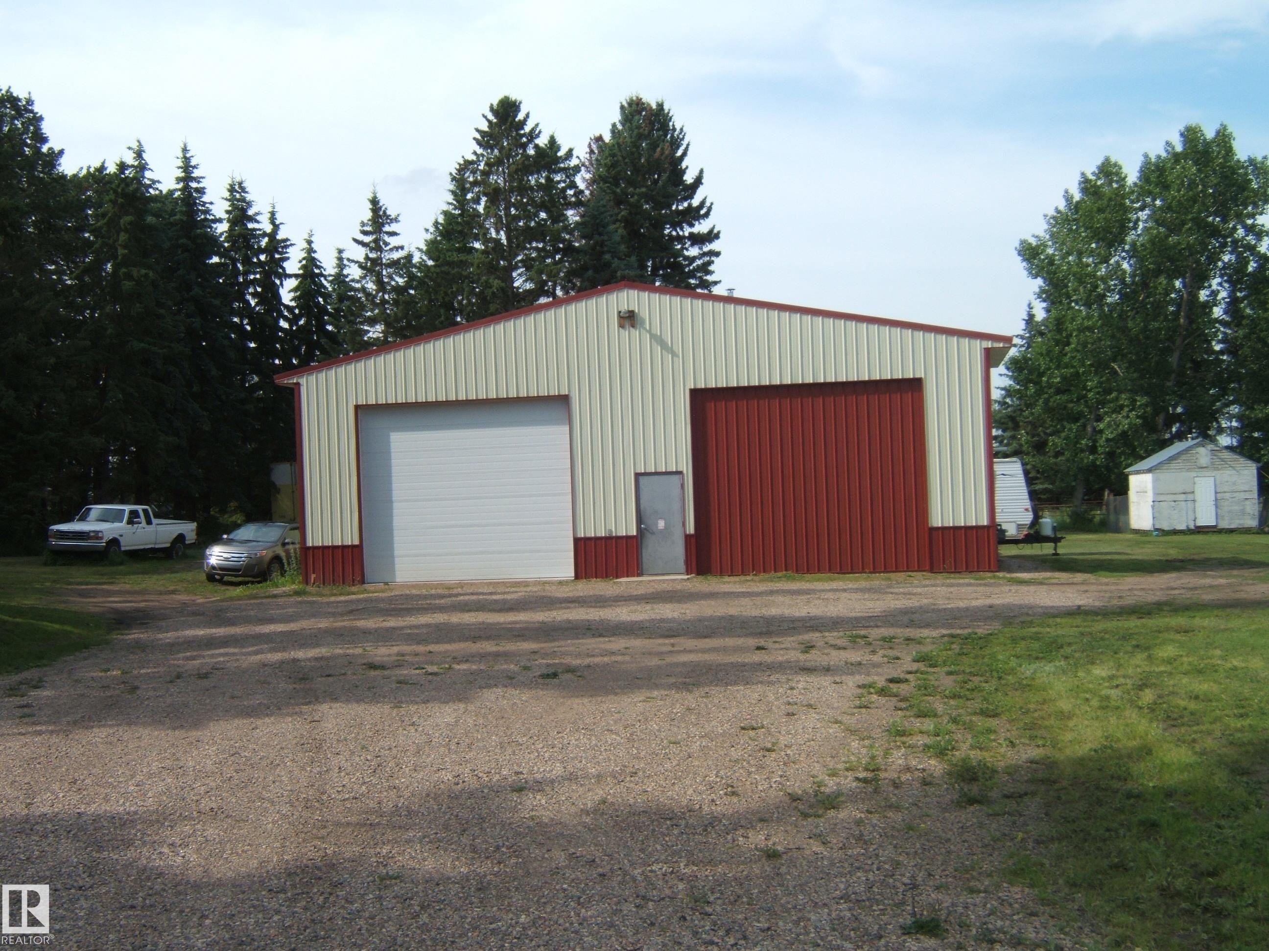 Metal outbuilding with a two-tone facade featuring red and off-white panels, a red roof trim, and a gravel driveway - 151042 Twp Rd 562, Rural Two Hills County, AB - Outdoor