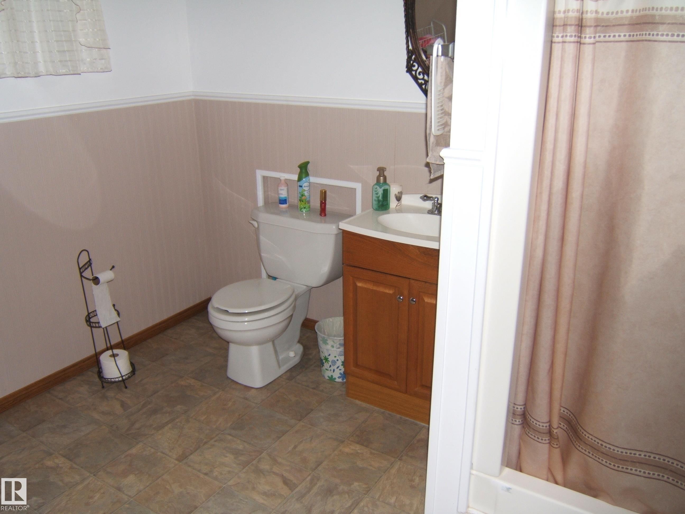 Bathroom featuring a white toilet, wood-finish vanity with an integrated sink, and a shower/tub combination - 151042 Twp Rd 562, Rural Two Hills County, AB - Indoor Photo Showing Bathroom