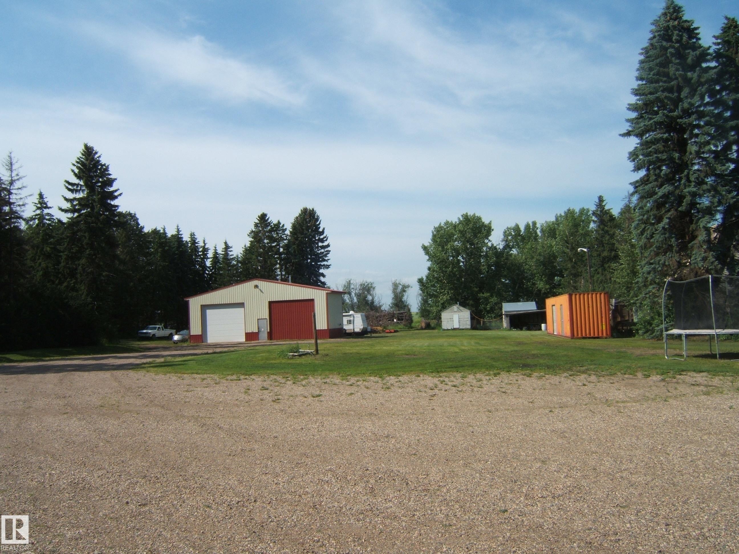 Gravel driveway with a large metal workshop featuring a roll-up door and side entry - 151042 Twp Rd 562, Rural Two Hills County, AB - Outdoor