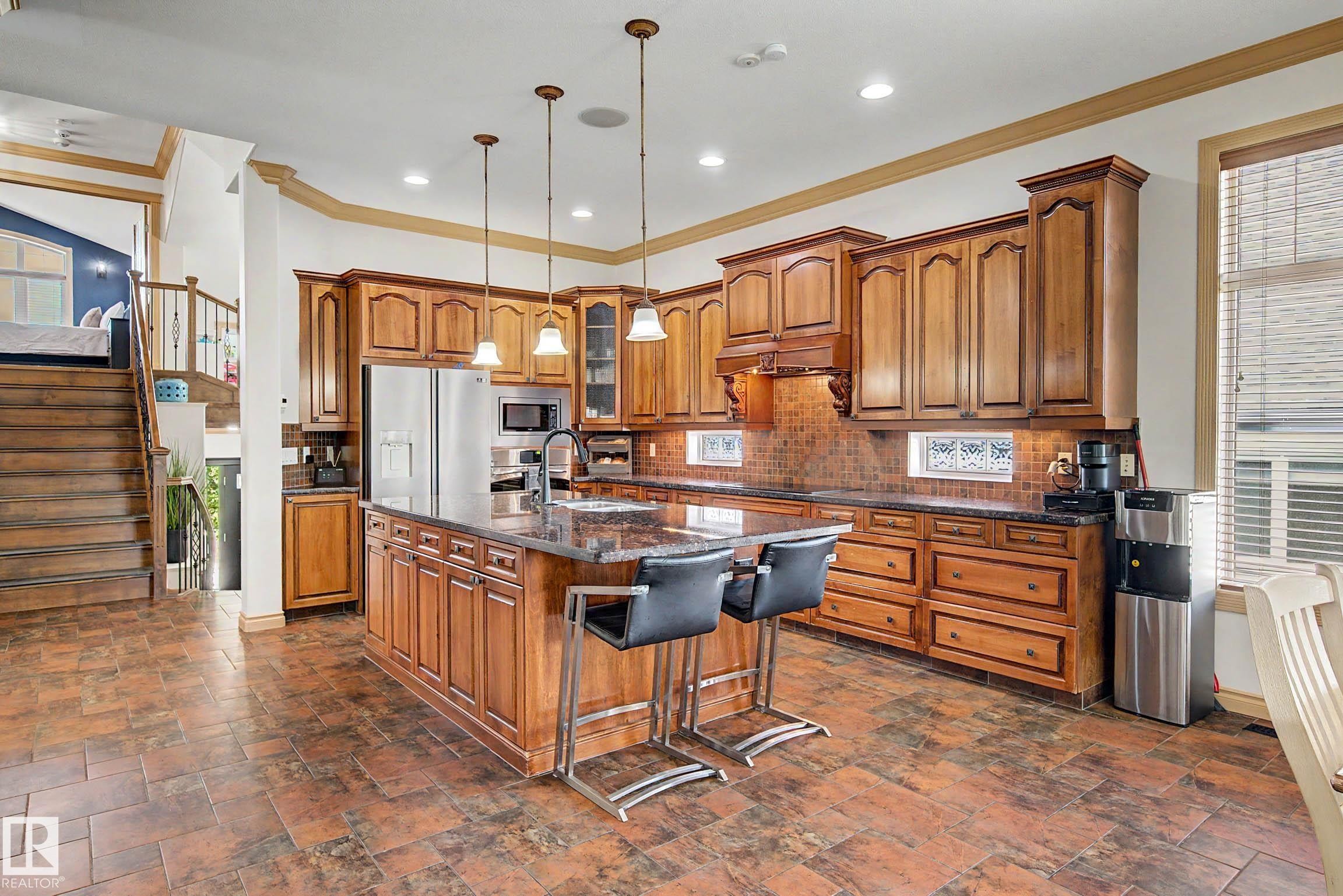 Gourmet kitchen featuring a large central island with seating, pendant lighting, extensive wood cabinetry, and stainless steel appliances - 38 Longview Point(E), Spruce Grove, AB - Indoor Photo Showing Kitchen