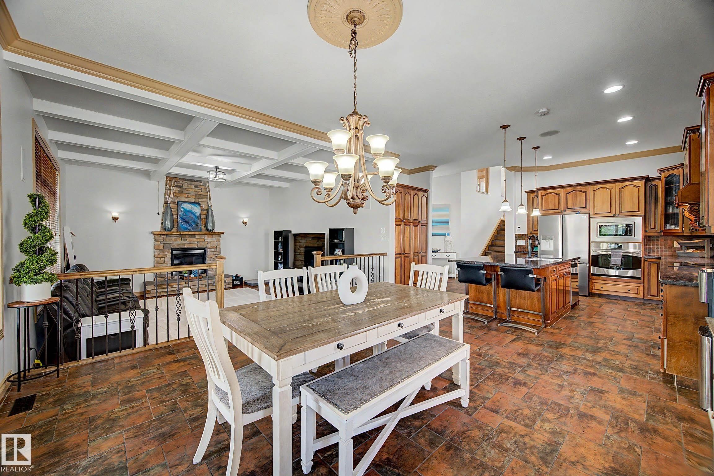 Open-concept living space featuring wood-finish flooring, a coffered ceiling, a stone fireplace, wood cabinetry, and a kitchen island with pendant lighting - 38 Longview Point(E), Spruce Grove, AB - Indoor Photo Showing Dining Room