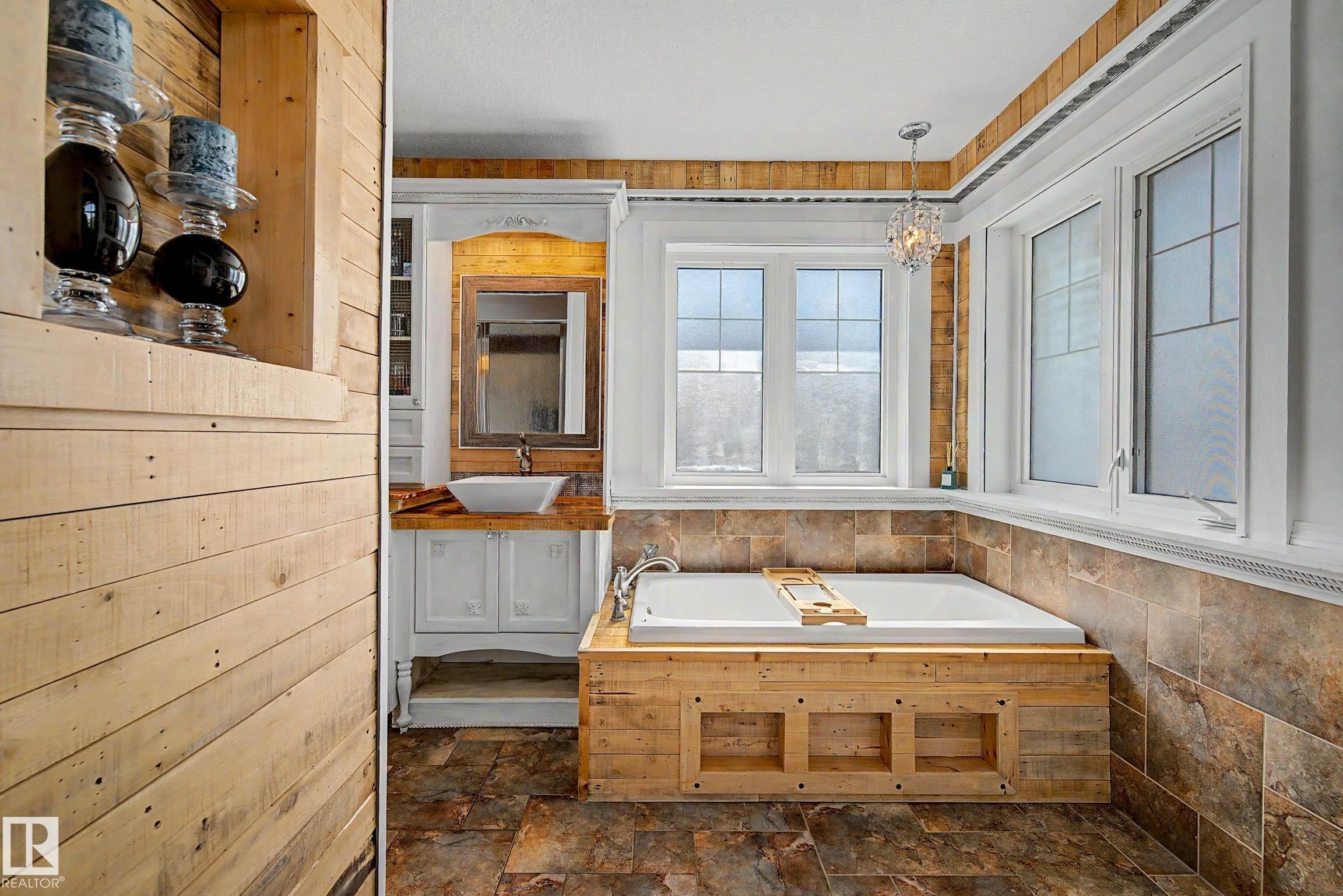 Spacious bathroom featuring a built-in soaking tub with a wood-finish surround, multiple large windows, and a crystalline chandelier - 38 Longview Point(E), Spruce Grove, AB - Indoor Photo Showing Bathroom