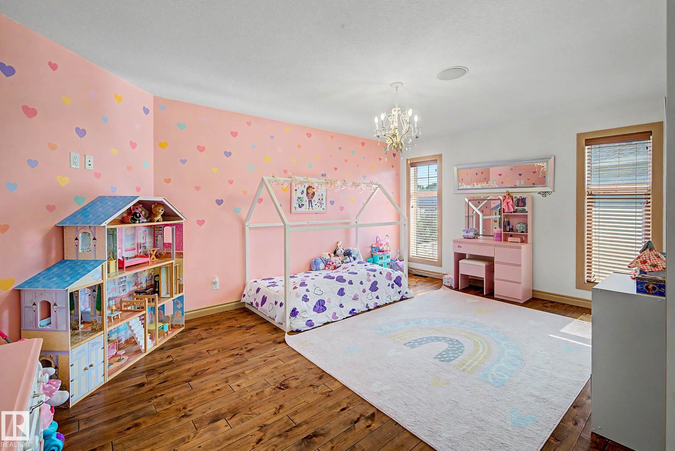 Bedroom featuring wood-finish flooring, two large windows with blinds, a crystal chandelier, and a decorative wall with heart-patterned wallpaper - 38 Longview Point(E), Spruce Grove, AB - Indoor Photo Showing Bedroom