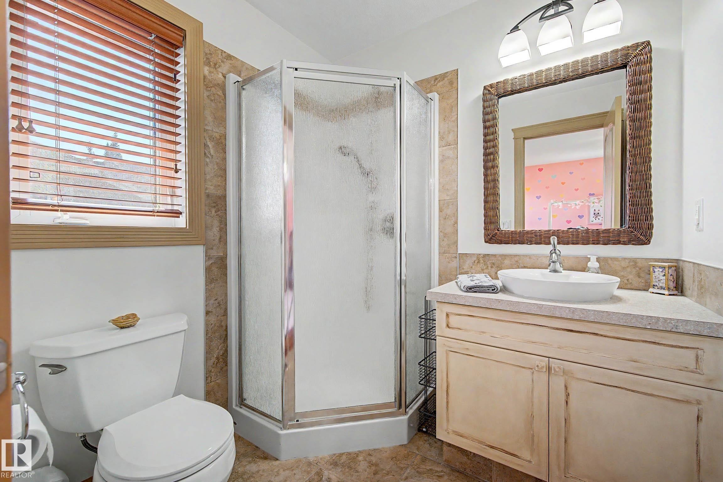 Bathroom featuring a corner shower enclosure, a single vanity with a vessel sink, a coordinating mirror, and wood-toned window blinds - 38 Longview Point(E), Spruce Grove, AB - Indoor Photo Showing Bathroom