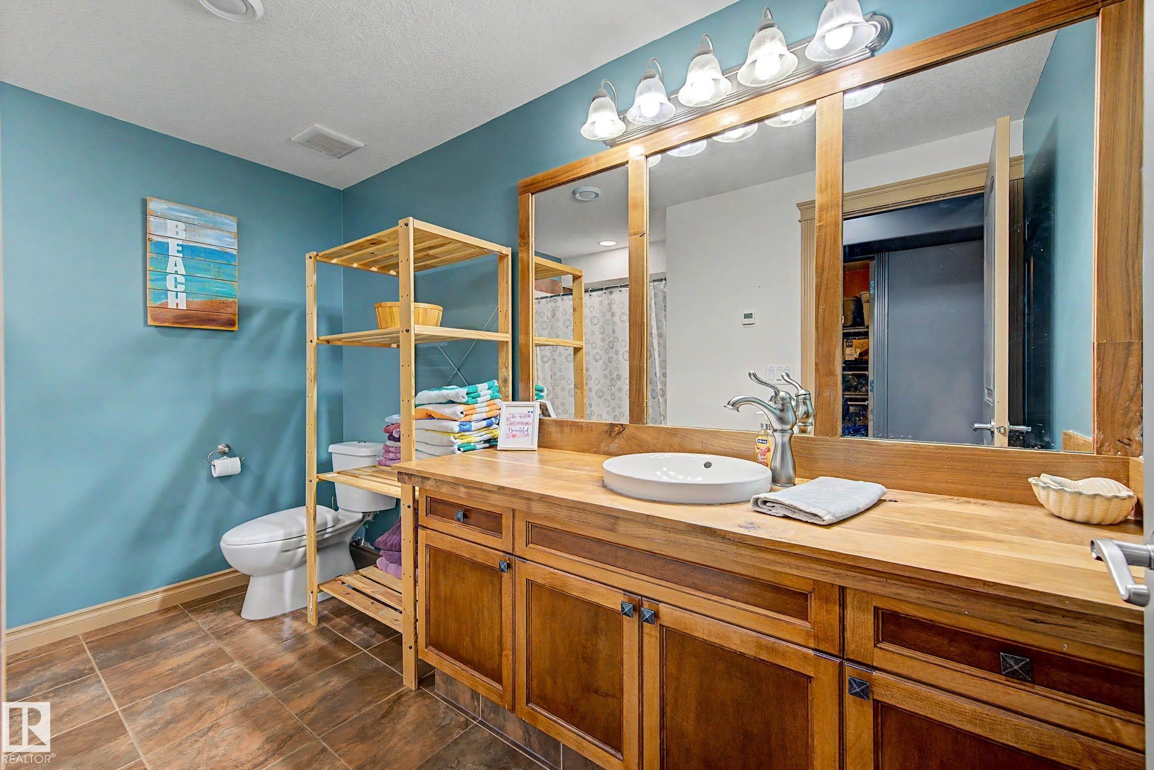 Bathroom featuring a wood-finish vanity with an oval vessel sink and a wall-mounted light fixture above a large mirror - 38 Longview Point(E), Spruce Grove, AB - Indoor Photo Showing Bathroom