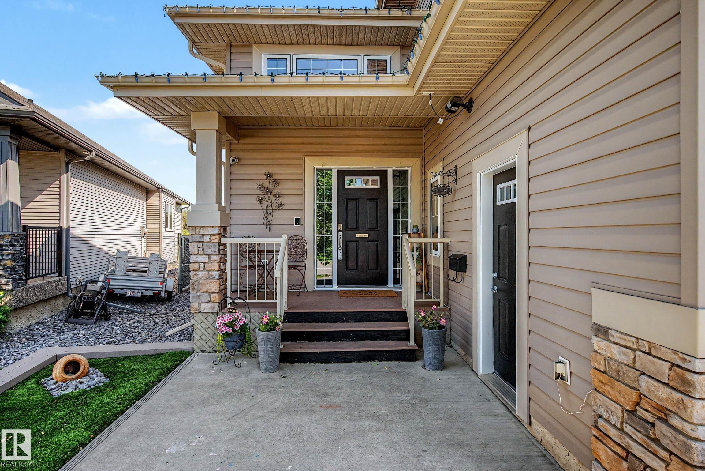 Inviting front entrance featuring a dark wood-finish door with sidelights, a covered porch with stone-clad columns, and a concrete walkway - 38 Longview Point(E), Spruce Grove, AB - Outdoor With Deck Patio Veranda