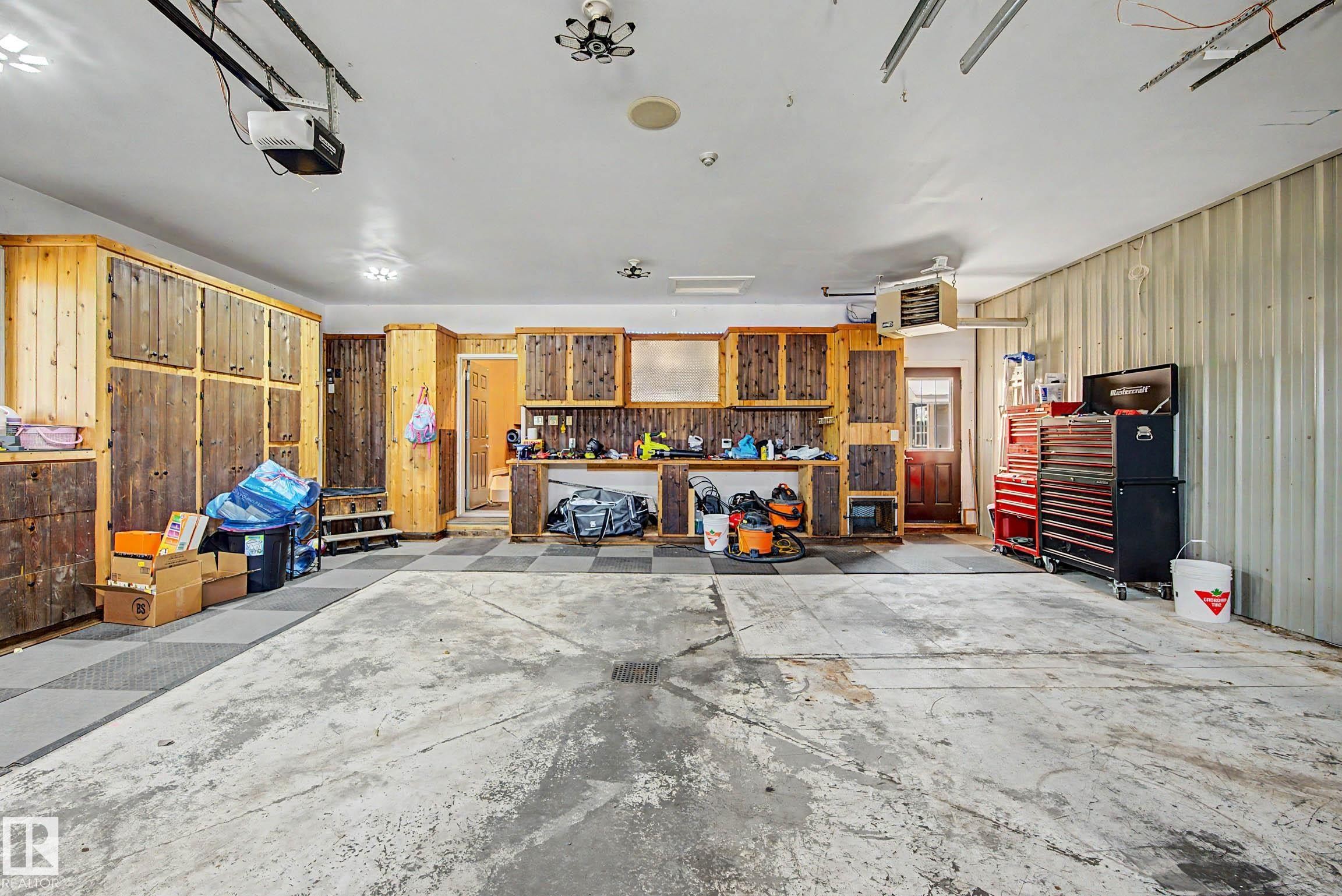 Spacious garage featuring extensive built-in wooden cabinetry, a dedicated workbench area, corrugated metal wall paneling, and a checkerboard pattern floor section - 38 Longview Point(E), Spruce Grove, AB - Indoor Photo Showing Garage