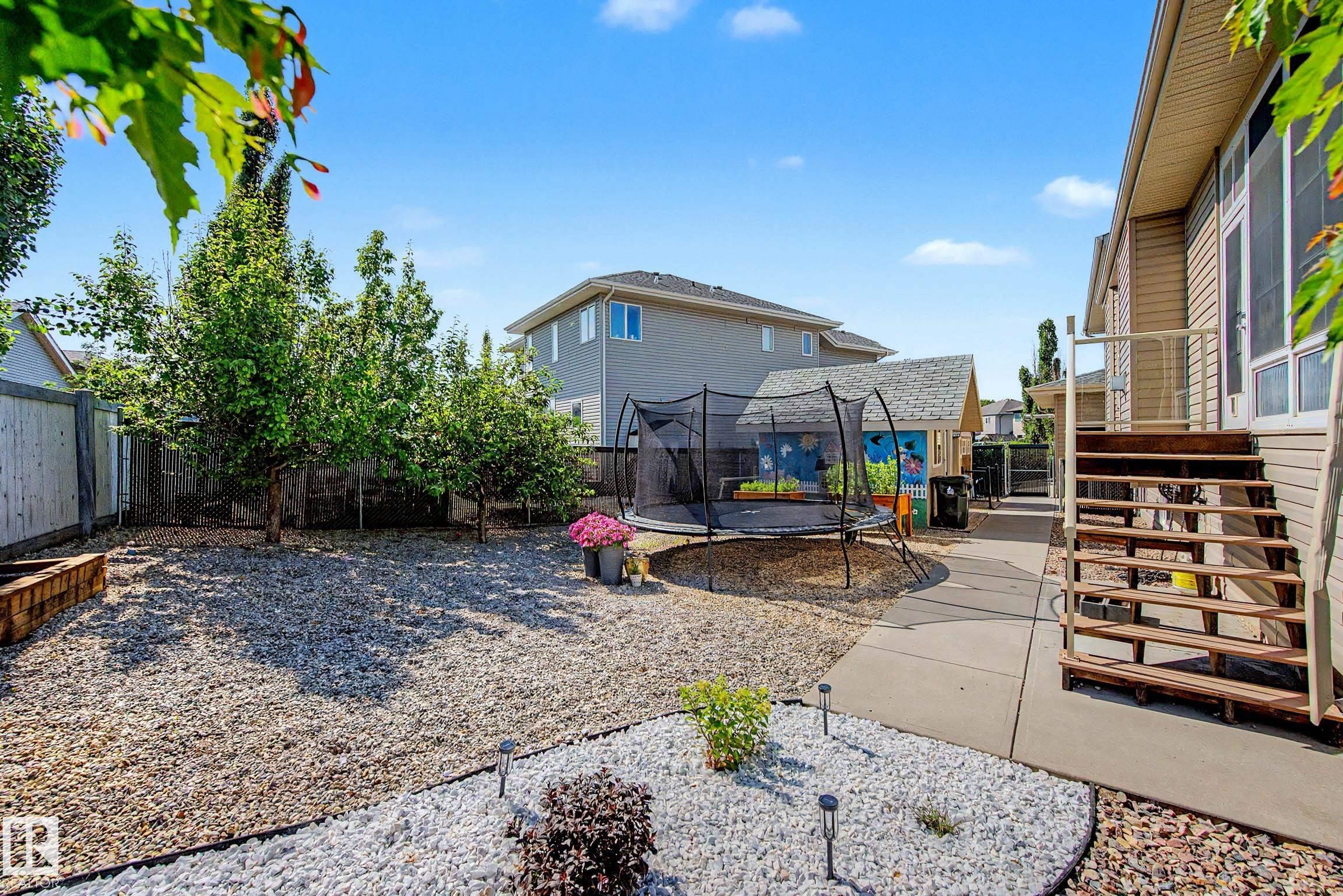 Landscaped backyard featuring gravel ground cover, mature trees, a concrete walkway, and exterior stairs leading to the property - 38 Longview Point(E), Spruce Grove, AB - Outdoor With Deck Patio Veranda