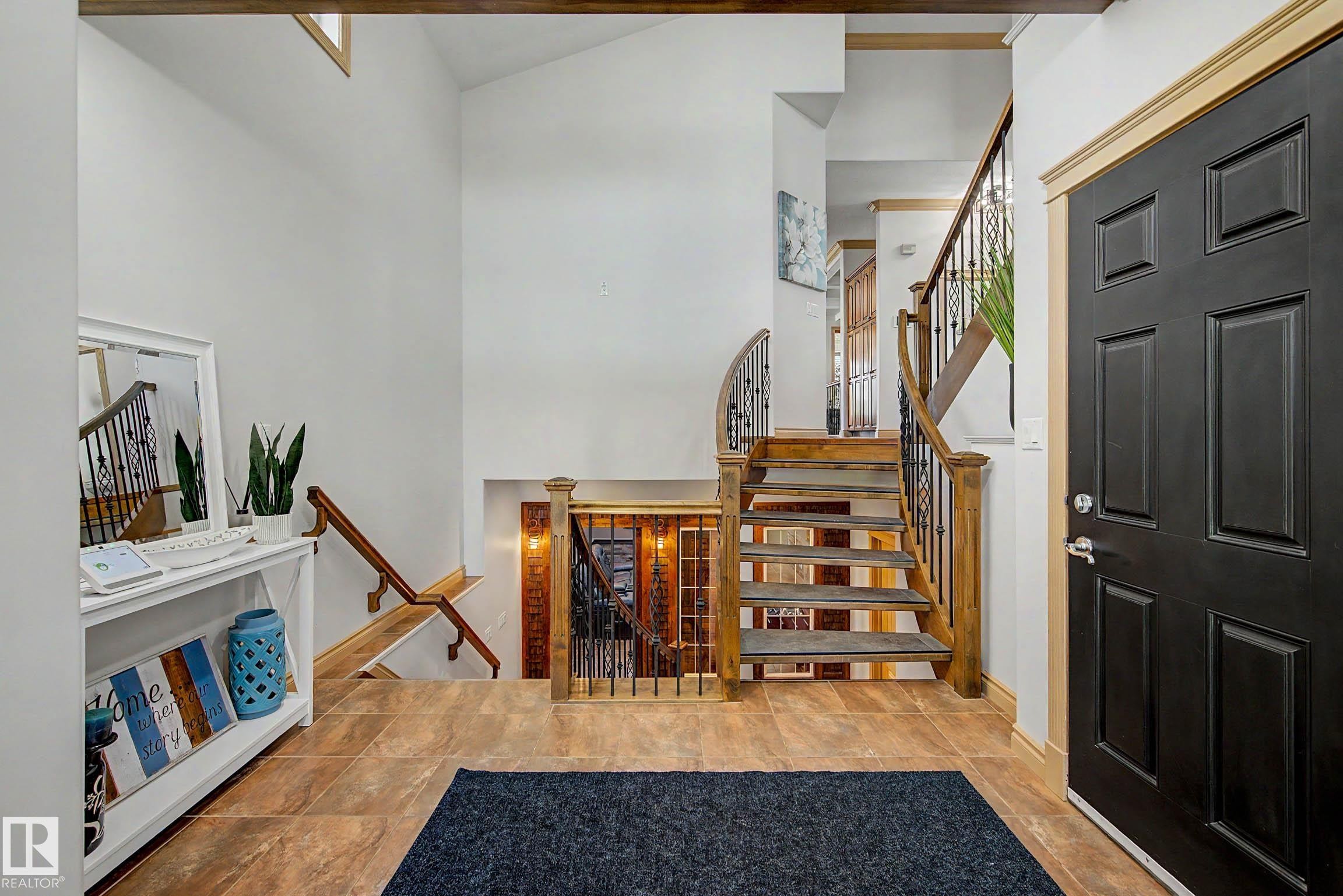 Entry foyer with a black paneled door and light wood trim, featuring a multi-level staircase with wood treads and wrought iron balusters - 38 Longview Point(E), Spruce Grove, AB - Indoor Photo Showing Other Room