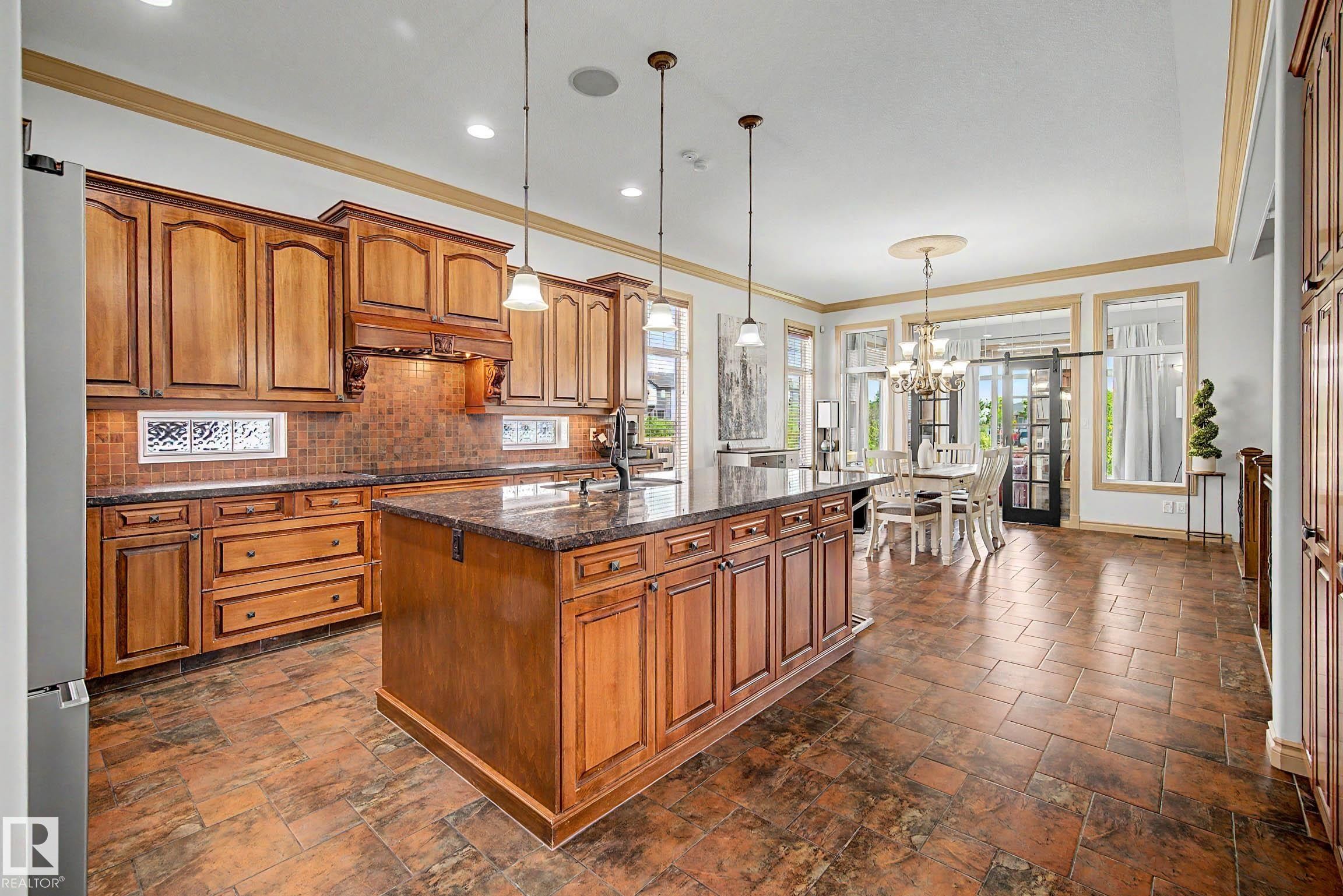 Spacious kitchen featuring warm wood cabinetry, a large center island with a stone-finish countertop, and tile flooring - 38 Longview Point(E), Spruce Grove, AB - Indoor Photo Showing Kitchen With Upgraded Kitchen