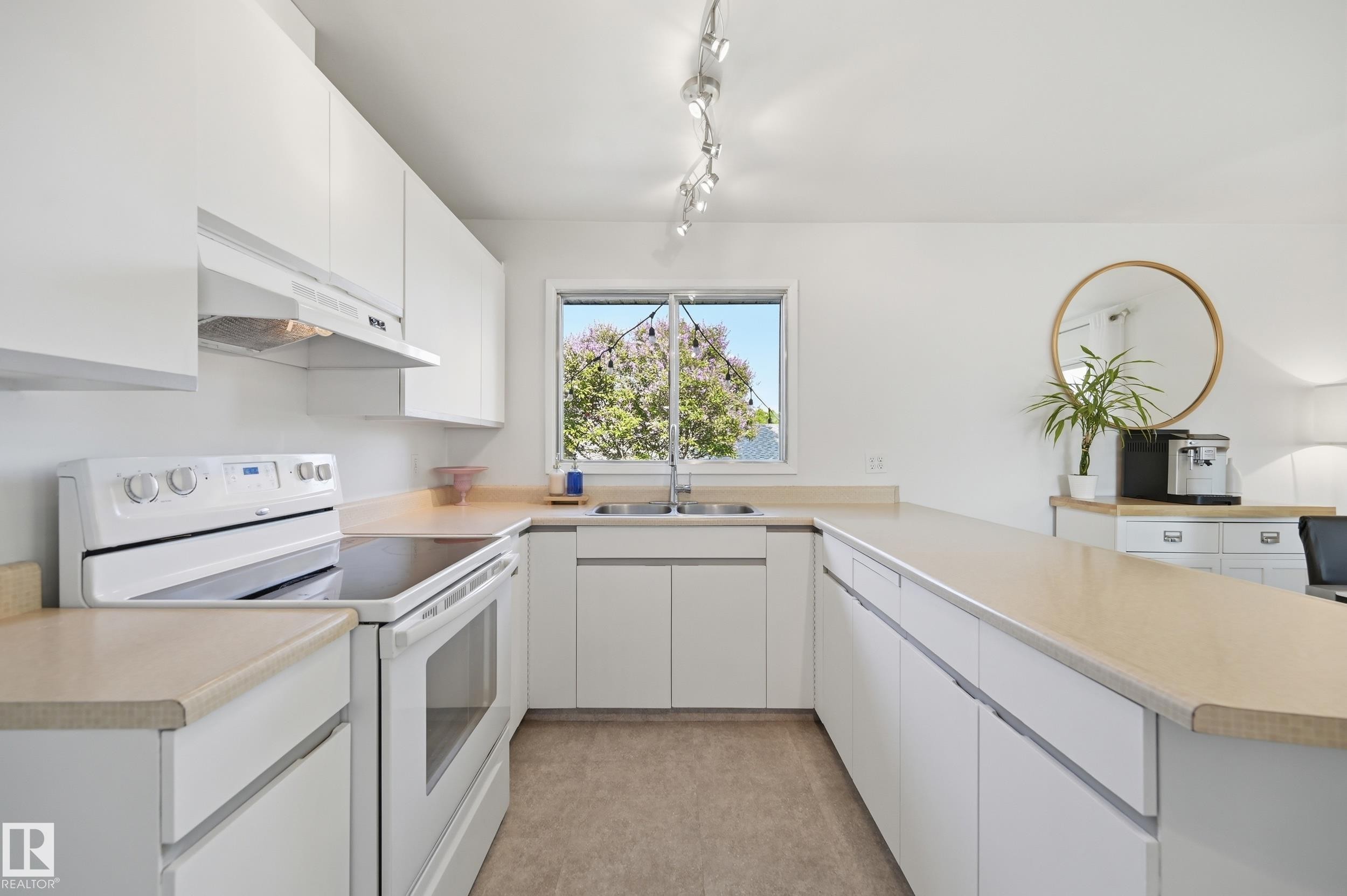 Bright kitchen featuring white cabinetry, light countertops, a window above the sink, a white electric range with an overhead vent, and track lighting - 15111 67 Street Nw, Edmonton, AB - Indoor Photo Showing Kitchen With Double Sink