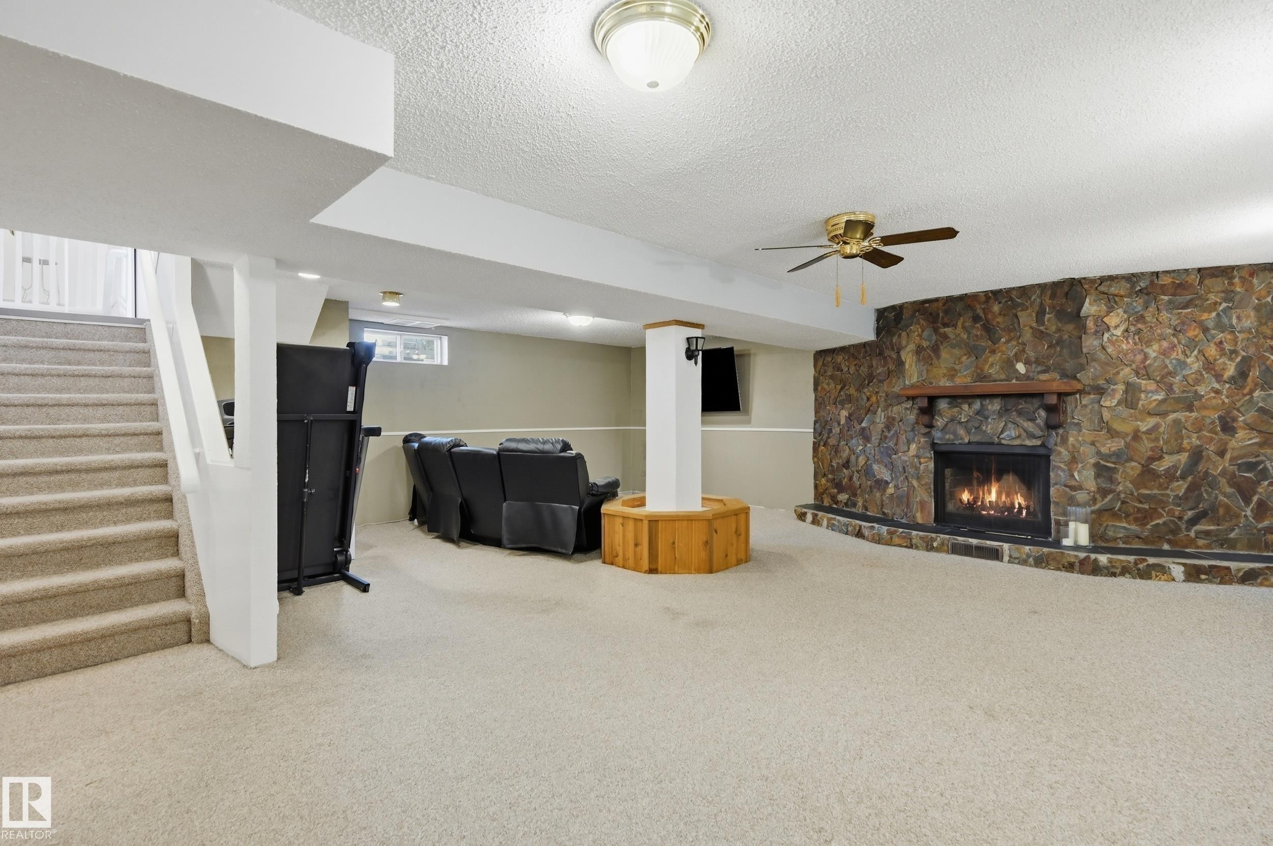 Carpeted basement recreation room featuring a stone-faced fireplace with a wood mantle, a ceiling fan, and recessed lighting - 15111 67 Street Nw, Edmonton, AB - Indoor With Fireplace