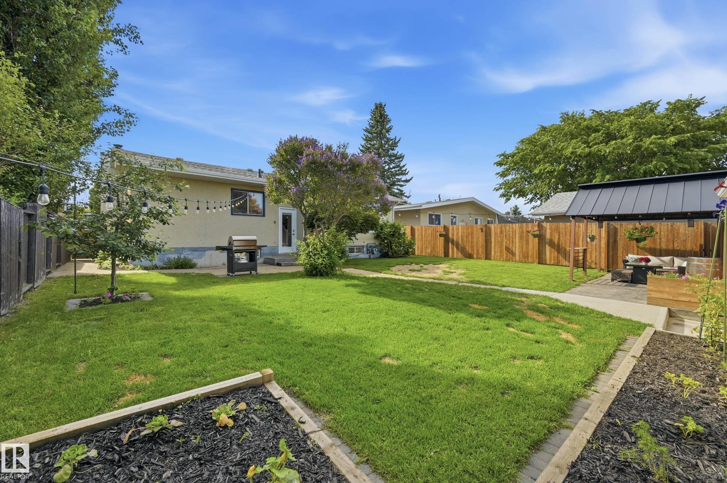 Expansive backyard featuring a manicured lawn, concrete patio, and garden beds - 15111 67 Street Nw, Edmonton, AB - Outdoor