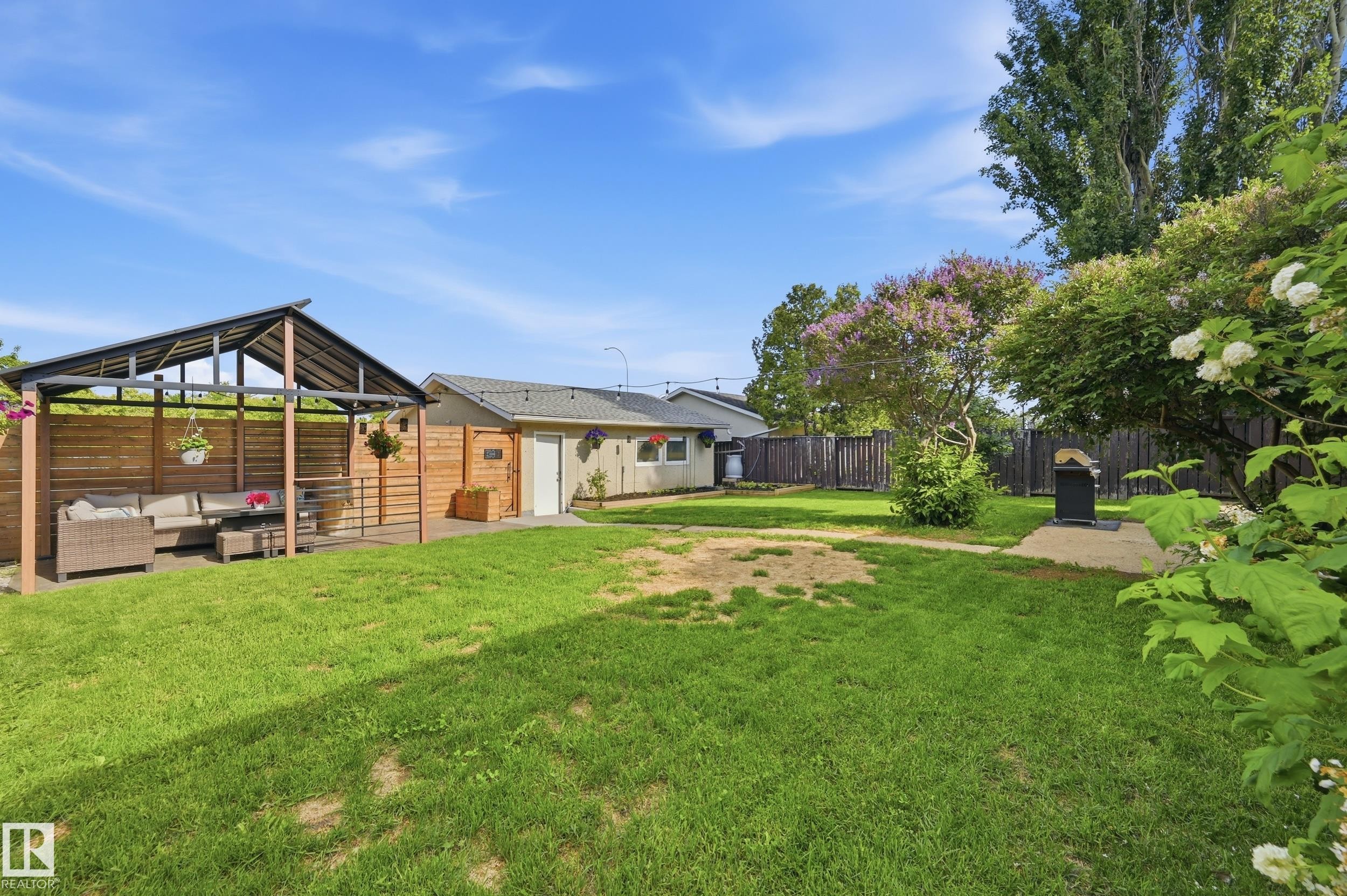 Expansive backyard featuring a covered patio structure, a privacy fence, a concrete pad, and mature flowering trees - 15111 67 Street Nw, Edmonton, AB - Outdoor