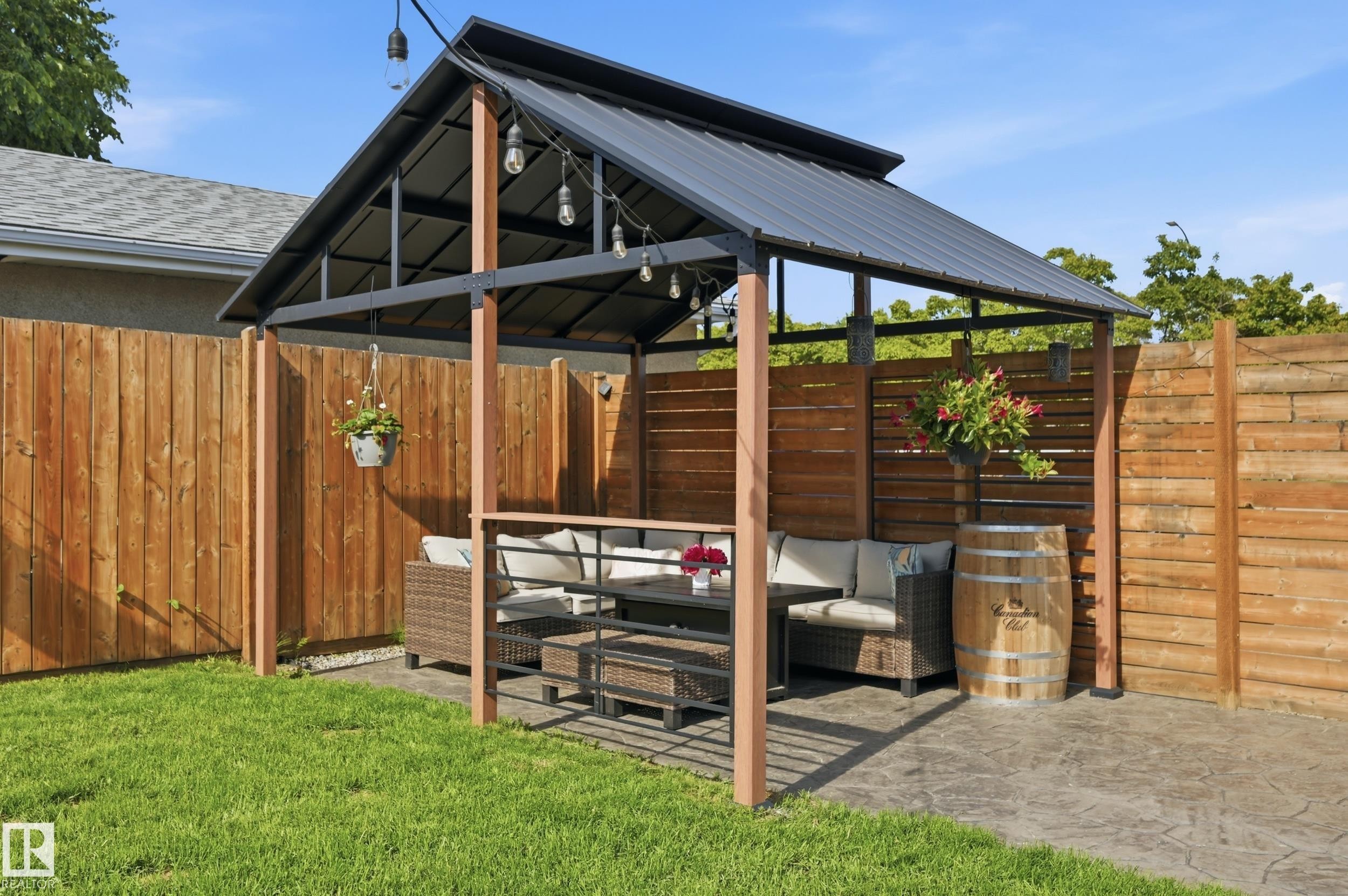 Private backyard space featuring a stamped concrete patio, a metal-roofed gazebo with integrated string lighting, and wood privacy fencing - 15111 67 Street Nw, Edmonton, AB - Outdoor With Exterior