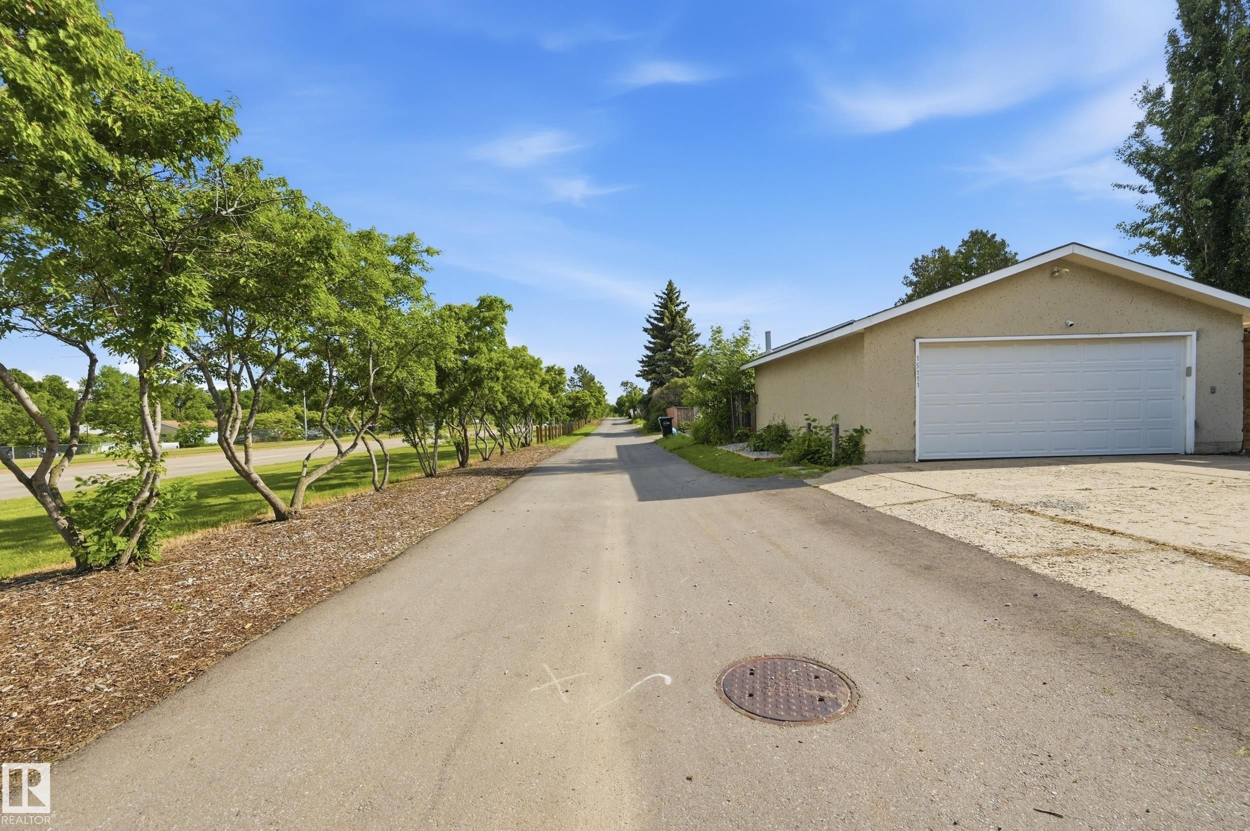 Detached garage with a white garage door, tan stucco exterior, and a peaked roofline - 15111 67 Street Nw, Edmonton, AB - Outdoor