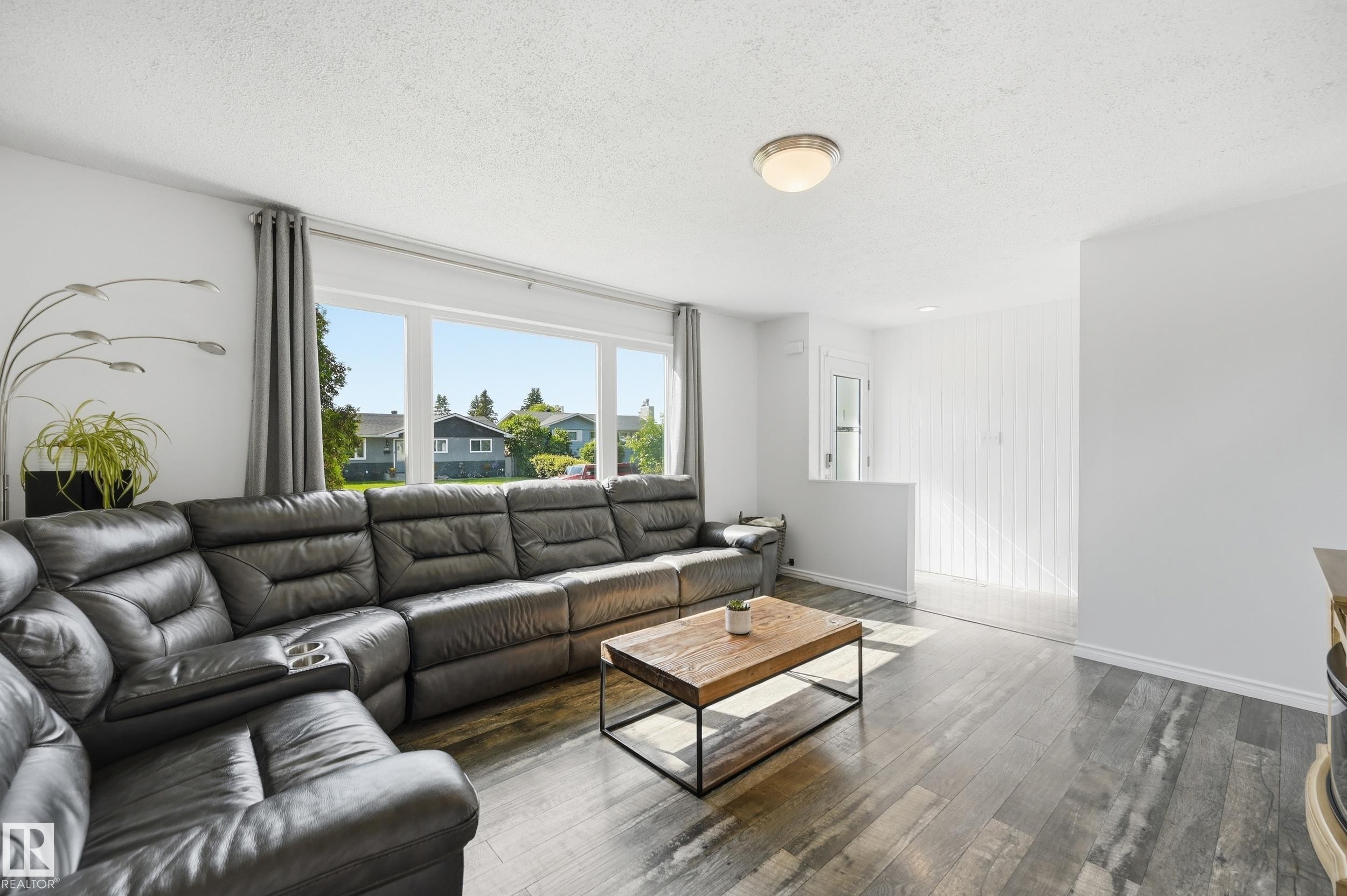 Spacious interior featuring large windows, wood-finish flooring, and white painted walls - 15111 67 Street Nw, Edmonton, AB - Indoor Photo Showing Living Room
