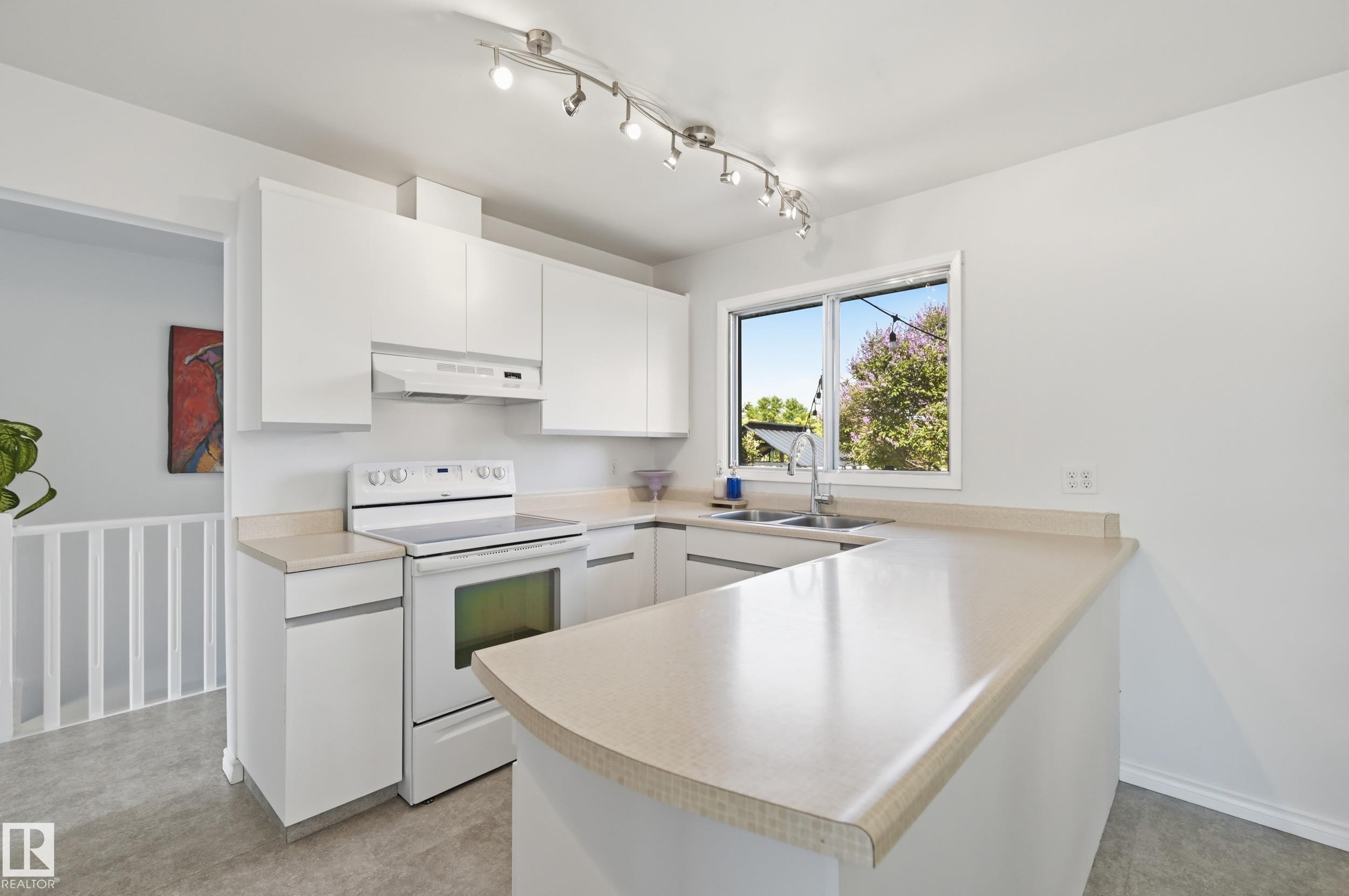 Modern kitchen featuring white cabinetry, a white electric range, and light-toned countertops - 15111 67 Street Nw, Edmonton, AB - Indoor Photo Showing Kitchen With Double Sink
