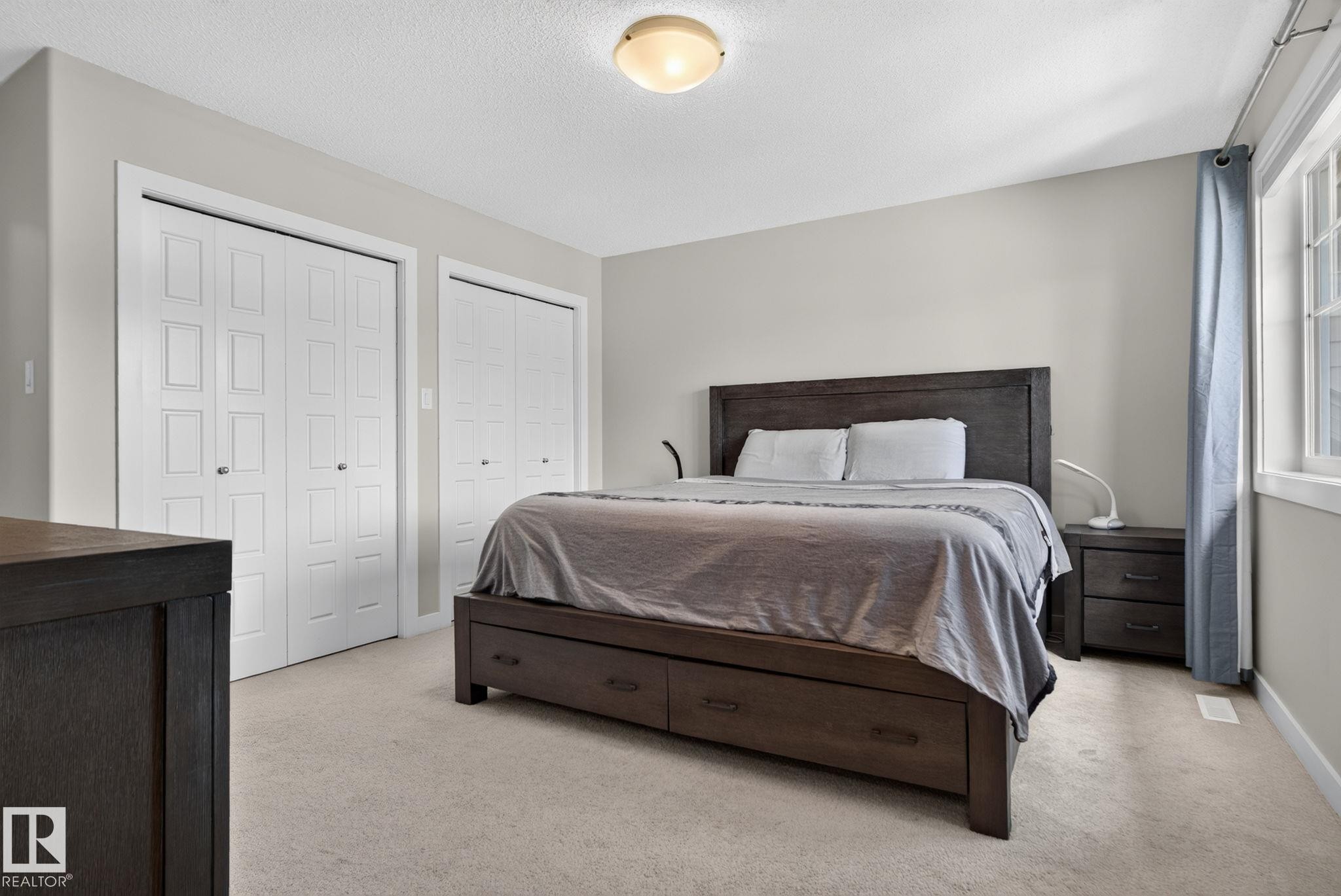 Bedroom featuring two sets of bi-fold closet doors, neutral wall paint, and carpet flooring - 319 Desrochers Boulevard Sw, Edmonton, AB - Indoor Photo Showing Bedroom