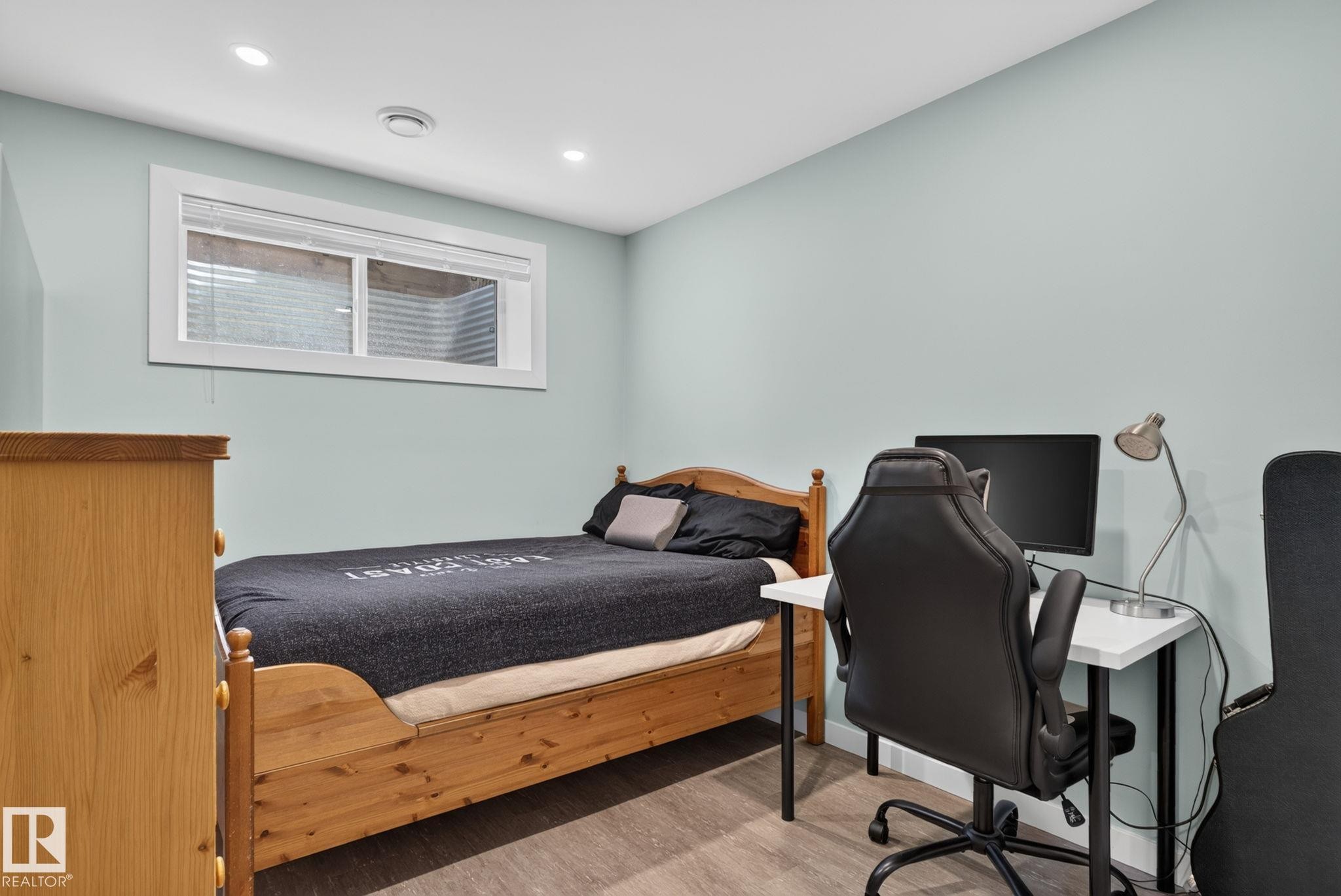 Room featuring light blue walls, wood-finish flooring, a wood-frame bed, and a window with white trim - 319 Desrochers Boulevard Sw, Edmonton, AB - Indoor Photo Showing Bedroom